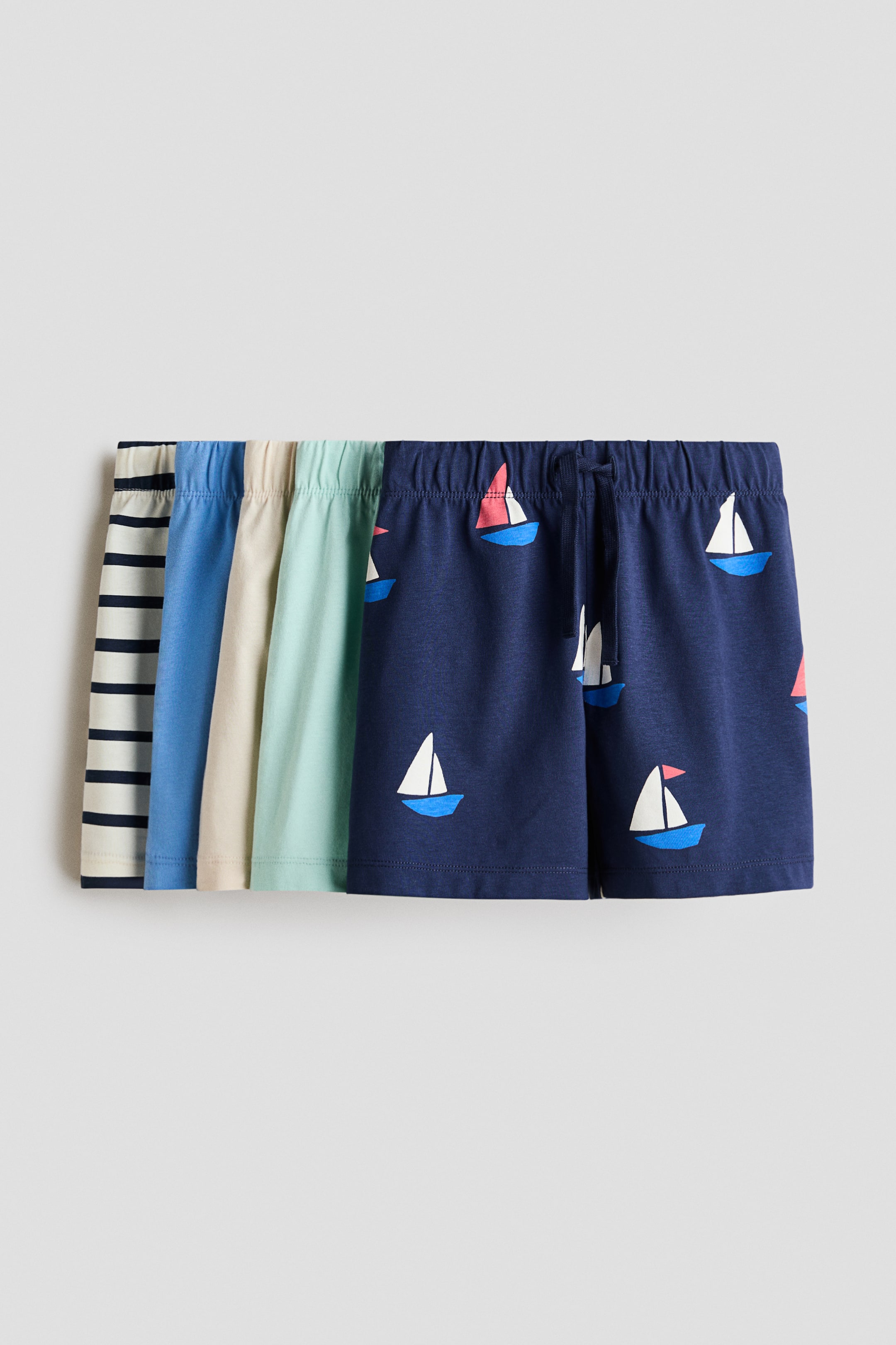 View larger image: A collection of soft cotton jersey knee-length shorts is displayed, with the foremost pair in a rich dark blue adorned with white and blue sailboat motifs. Each pair of shorts features a convenient pull-on waist with concealed elastication, and the dark blue pair is also equipped with a visible drawstring at the front.
