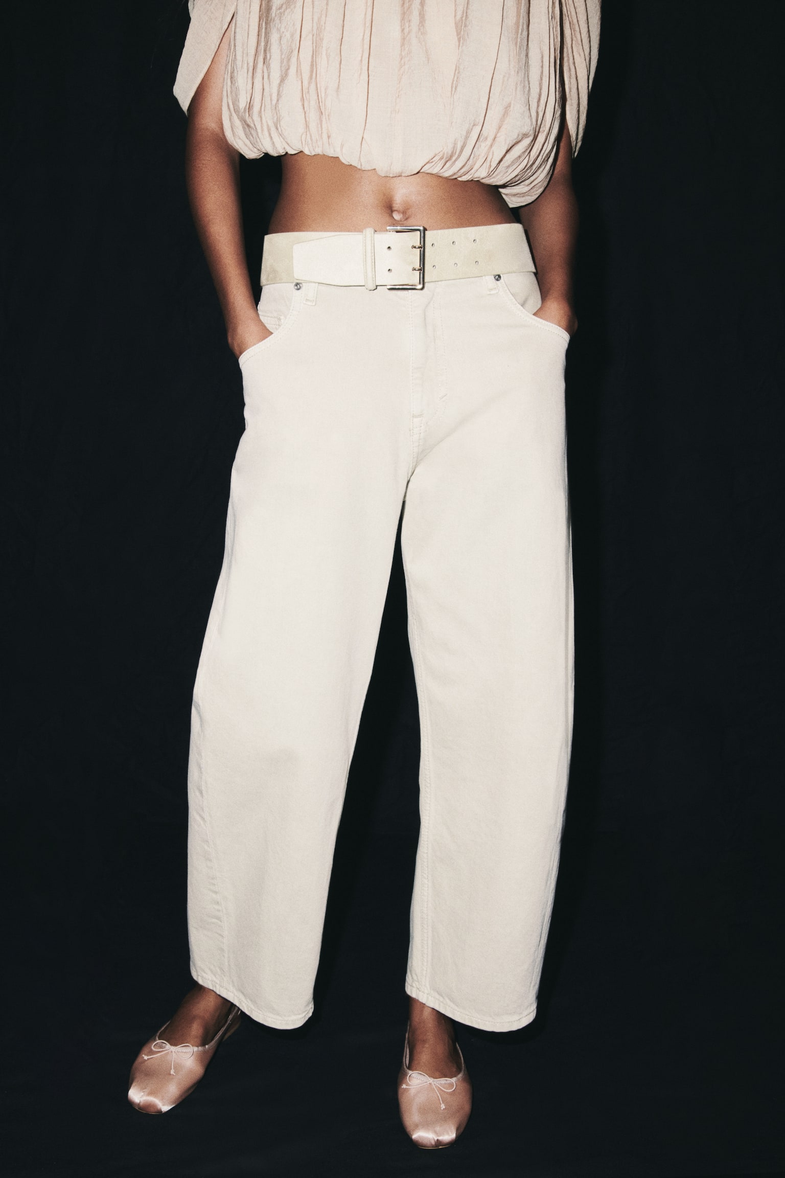 The beige wide-leg jeans are shown from the front, highlighting a button and zip fastening at the waist. Two curved front pockets and a small coin pocket are visible, complemented by prominent stitching details throughout the relaxed-fit garment. - 1