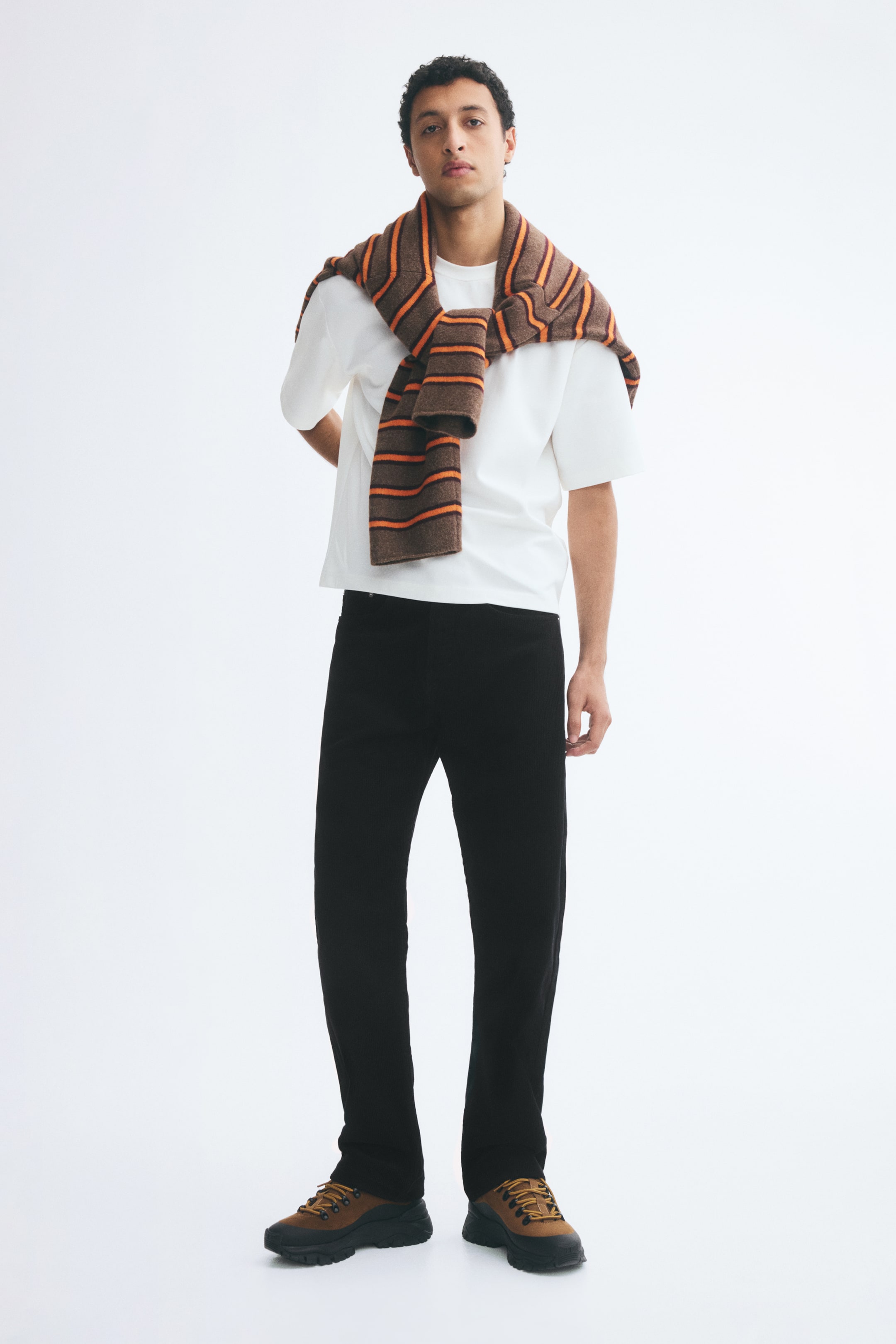 Größeres Bild anzeigen: Der/die Model trägt eine schwarze Cordhose in Regular Fit mit geradem Bein in Schwarz. Die Hose mit klassischer Silhouette ist mit einem weißen T-Shirt und braunen Schnürschuhen kombiniert.