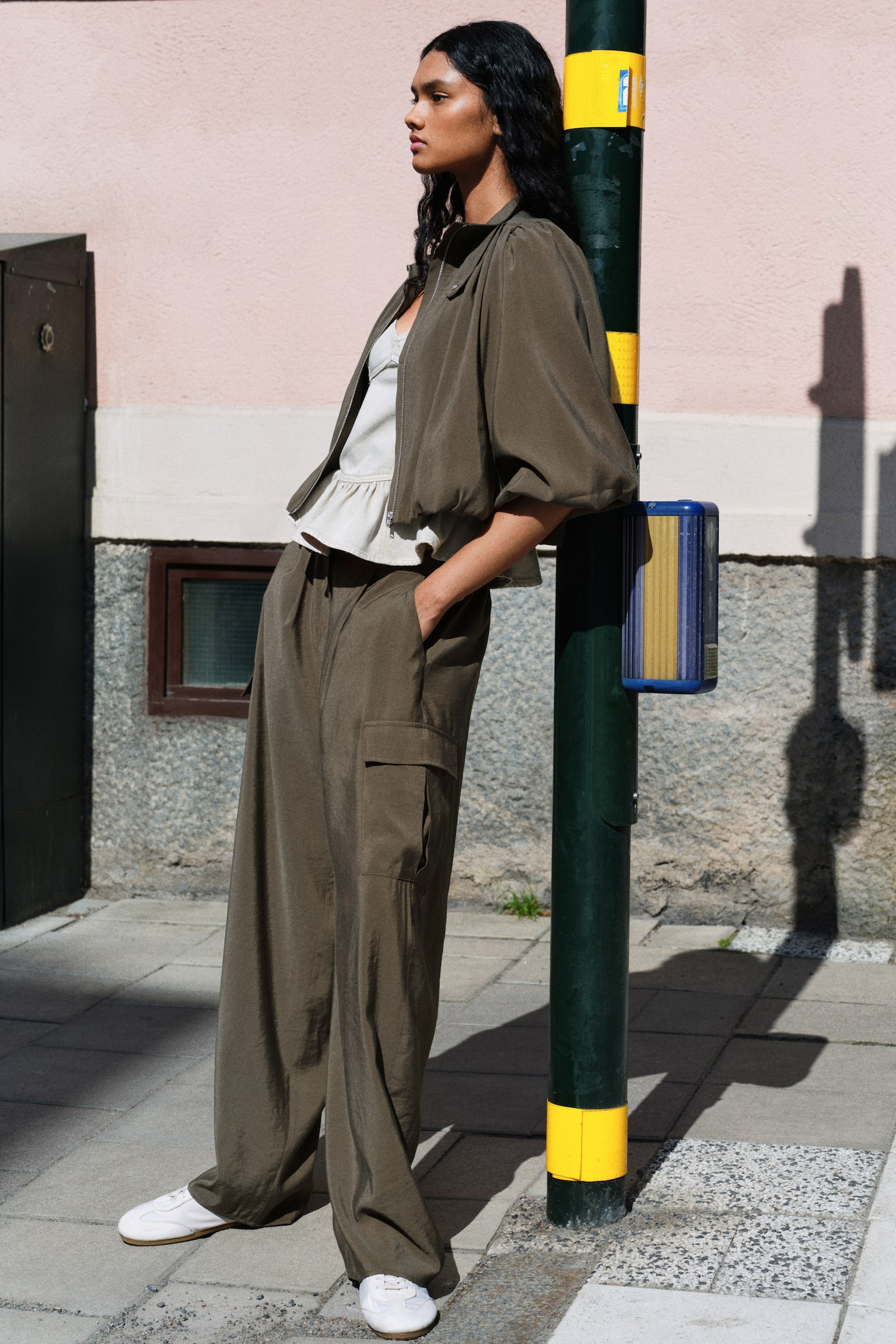 Dark olive green trousers are showcasing a front view, boasting a flat waistband, a central front seam, subtle pleats, and flap cargo pockets on each wide leg. - 1