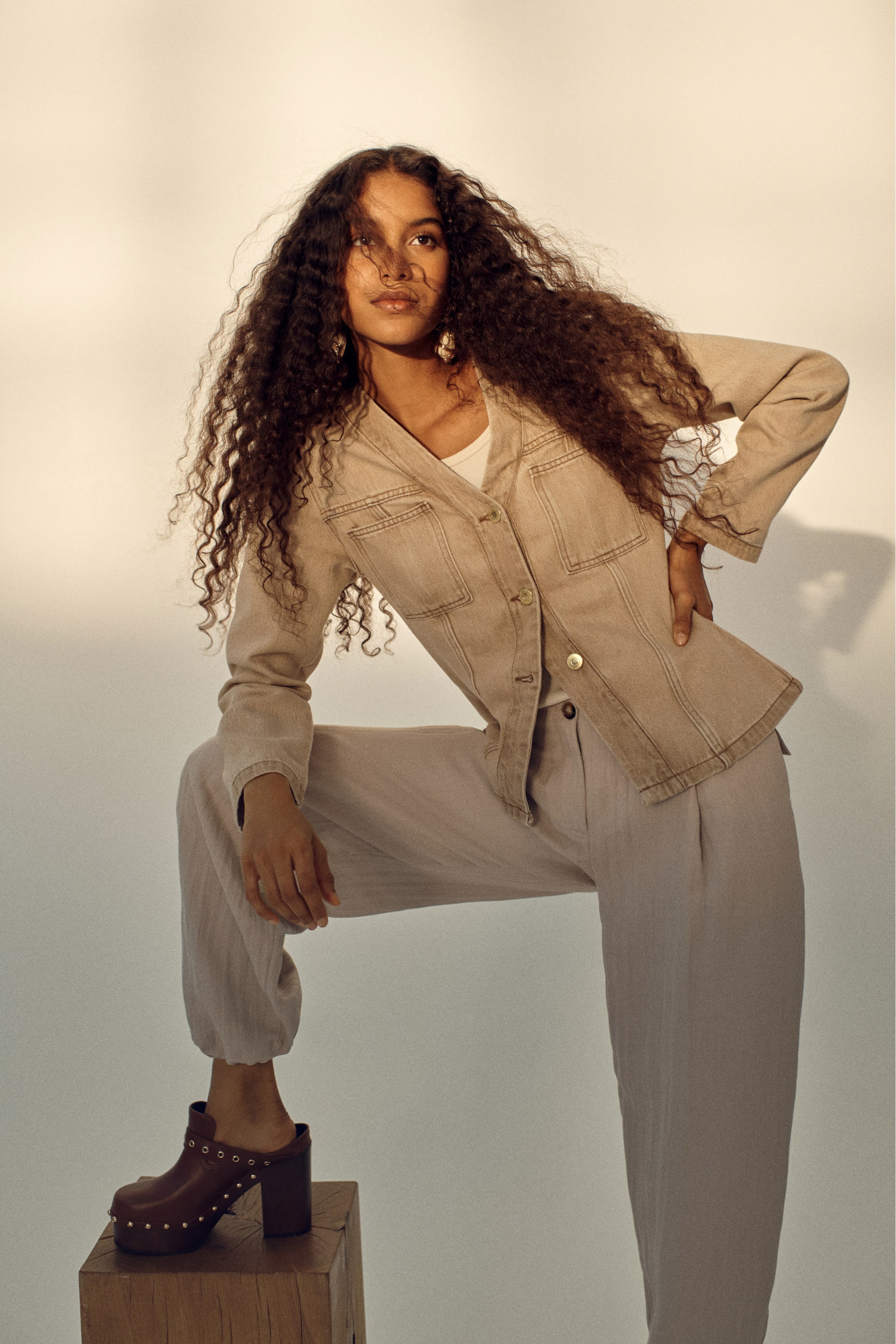 View larger image: A beige denim jacket featuring a V-neckline and two visible front buttons, layered over a white top. It also shows two chest flap pockets with button closures and visible seam detailing, angled slightly to the right.