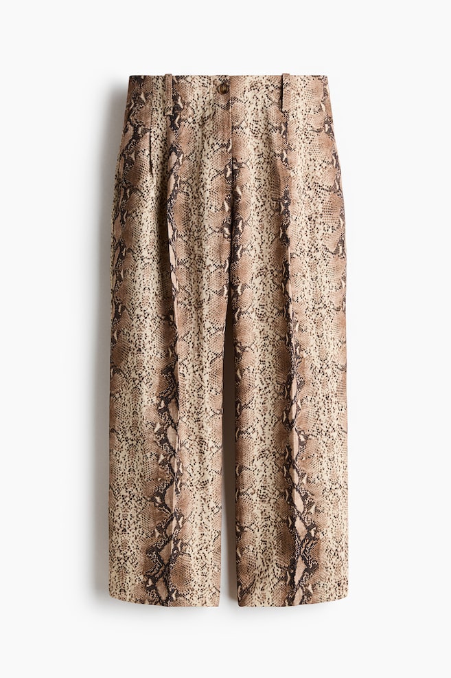 These front-facing, ankle-length, loose-fit trousers are displaying a snakeskin pattern in light brown and dark brown tones. They are featuring a regular waist with a visible button closure, front pleats, and diagonal side pockets. Vertical creases are running down the center of each straight leg. - 1