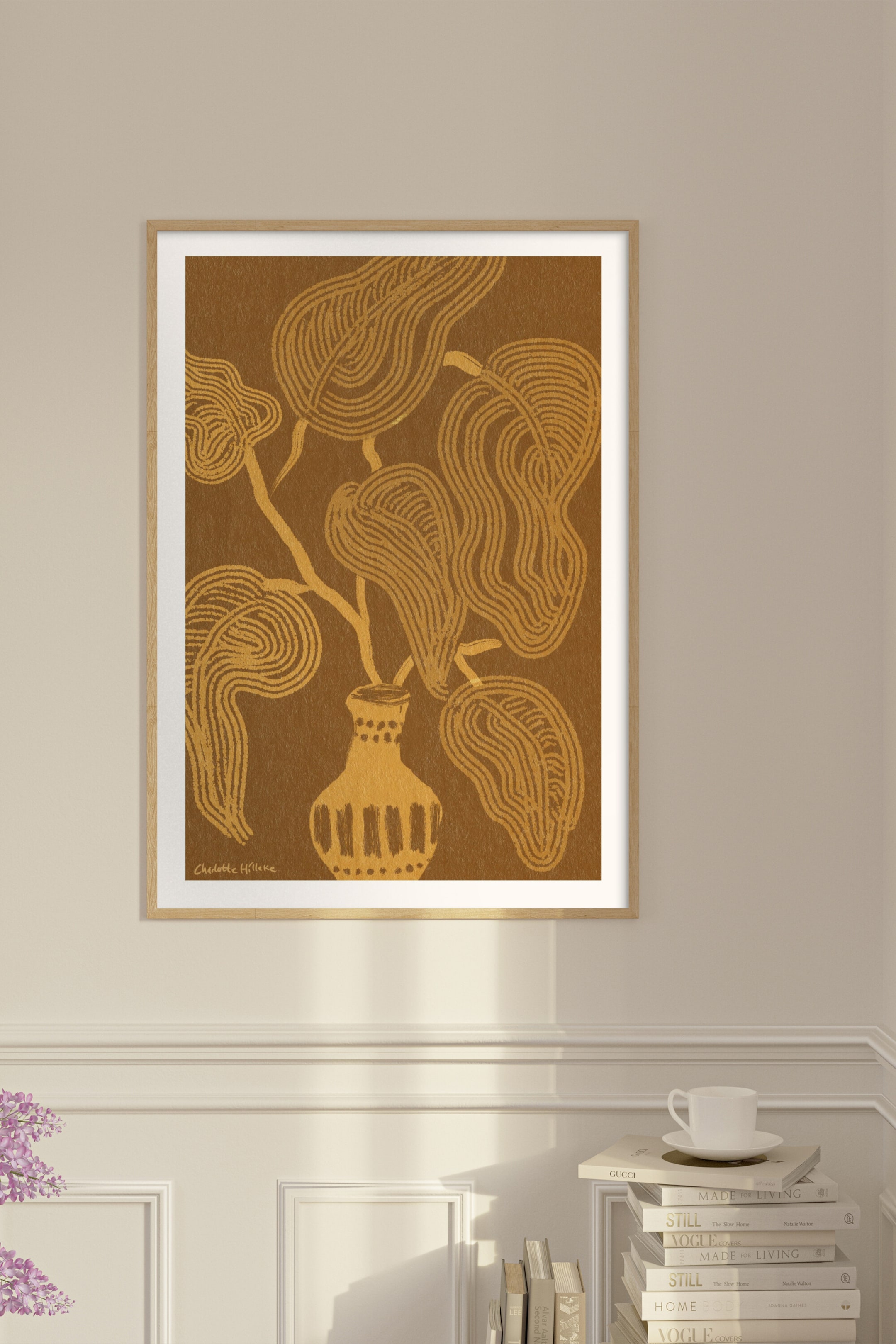 Agrandir l'image: Une impression d'art encadrée présente une illustration botanique abstraite de Charlotte Hilleke, représentant une plante aux feuilles dorées et fluides émergeant d'un vase à motifs. L'œuvre est posée sur un fond brun chaud et est encadrée par un cadre en bois clair avec un passe-partout blanc.