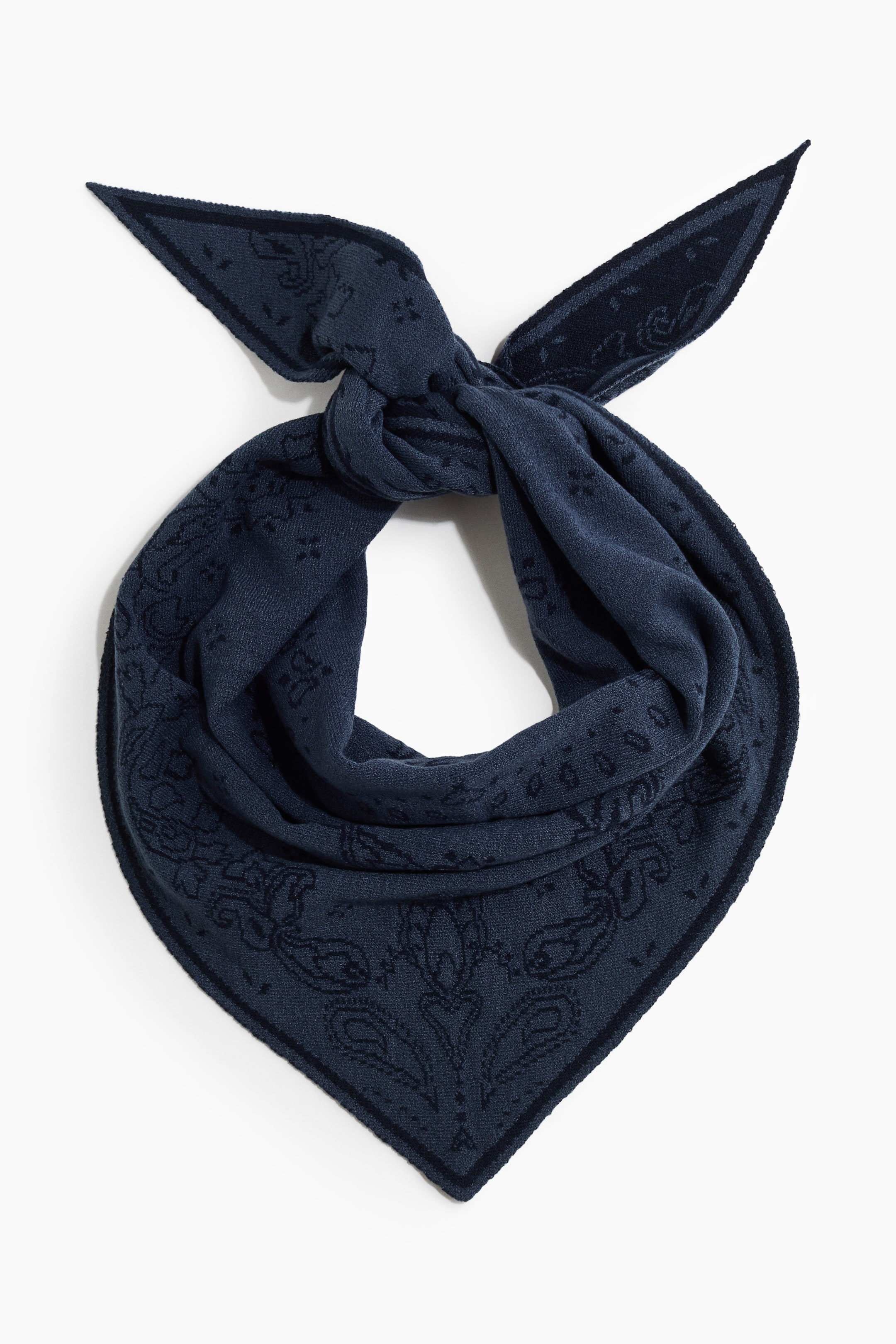 View larger image: A navy blue knit bandana is showing a subtle paisley pattern in matching tones with a solid dark border. It is shown from the front, styled in a draped triangular loop with a knot at the top and pointed ends extending outward.