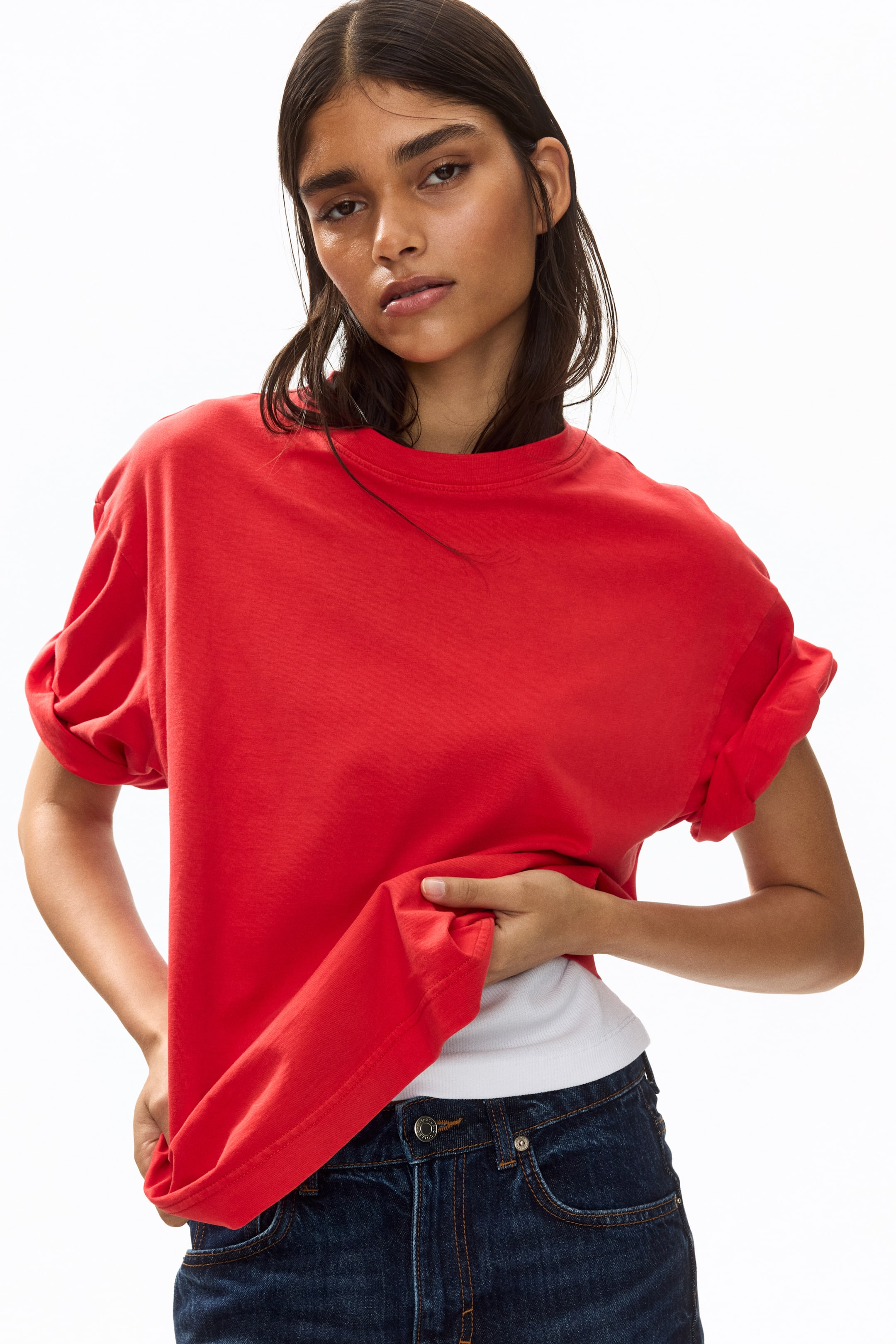View larger image: This red crew neck t-shirt boasts a relaxed fit, complete with rolled-up short sleeves. The front hem is stylishly lifted to showcase a white undershirt underneath.