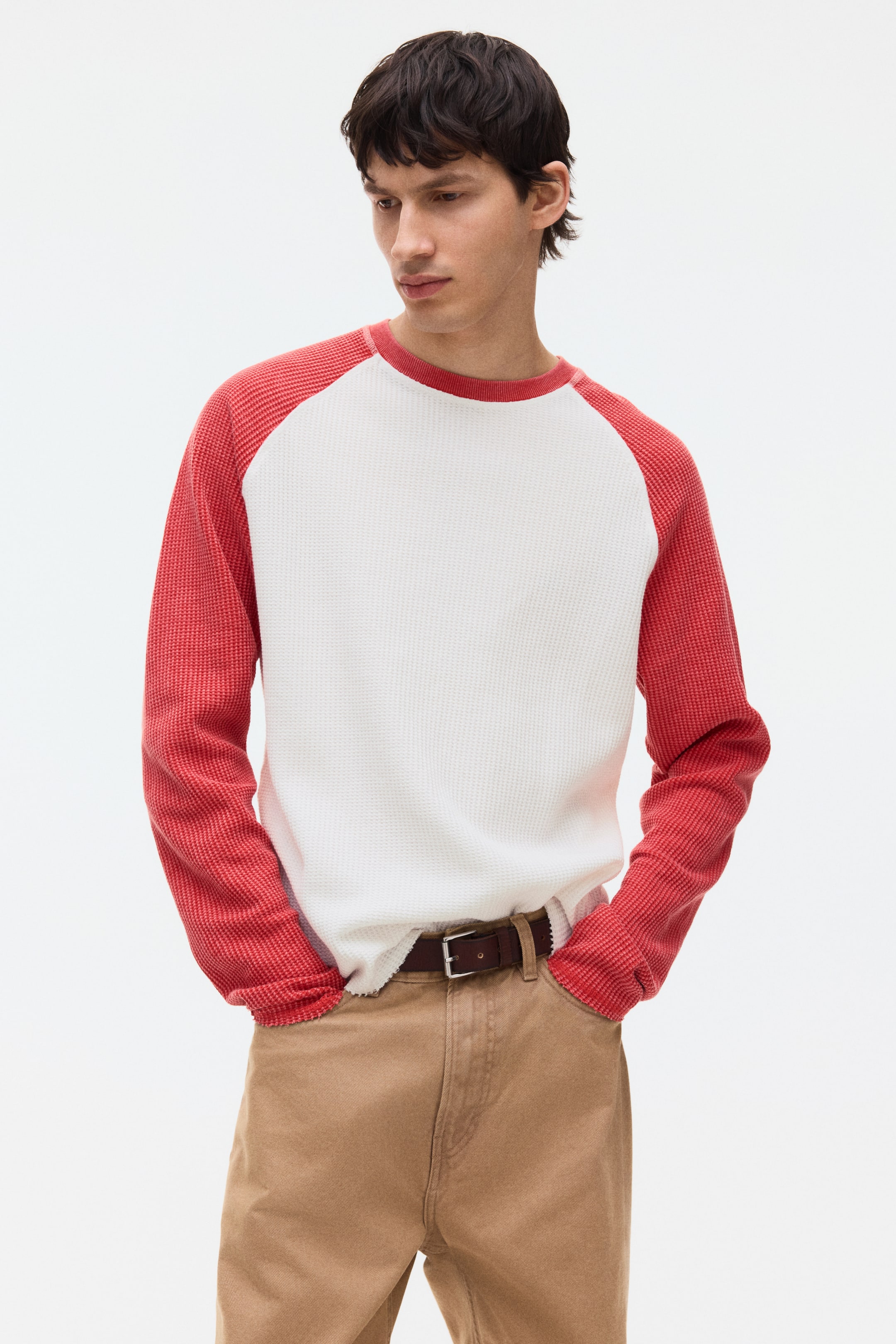 View larger image: Presenting a two-tone raglan long-sleeved waffle-knit shirt, showcasing an off-white body paired with reddish-orange raglan sleeves and a matching crew neck trim. The shirt is stylishly half-tucked into brown trousers, revealing its neat hem.