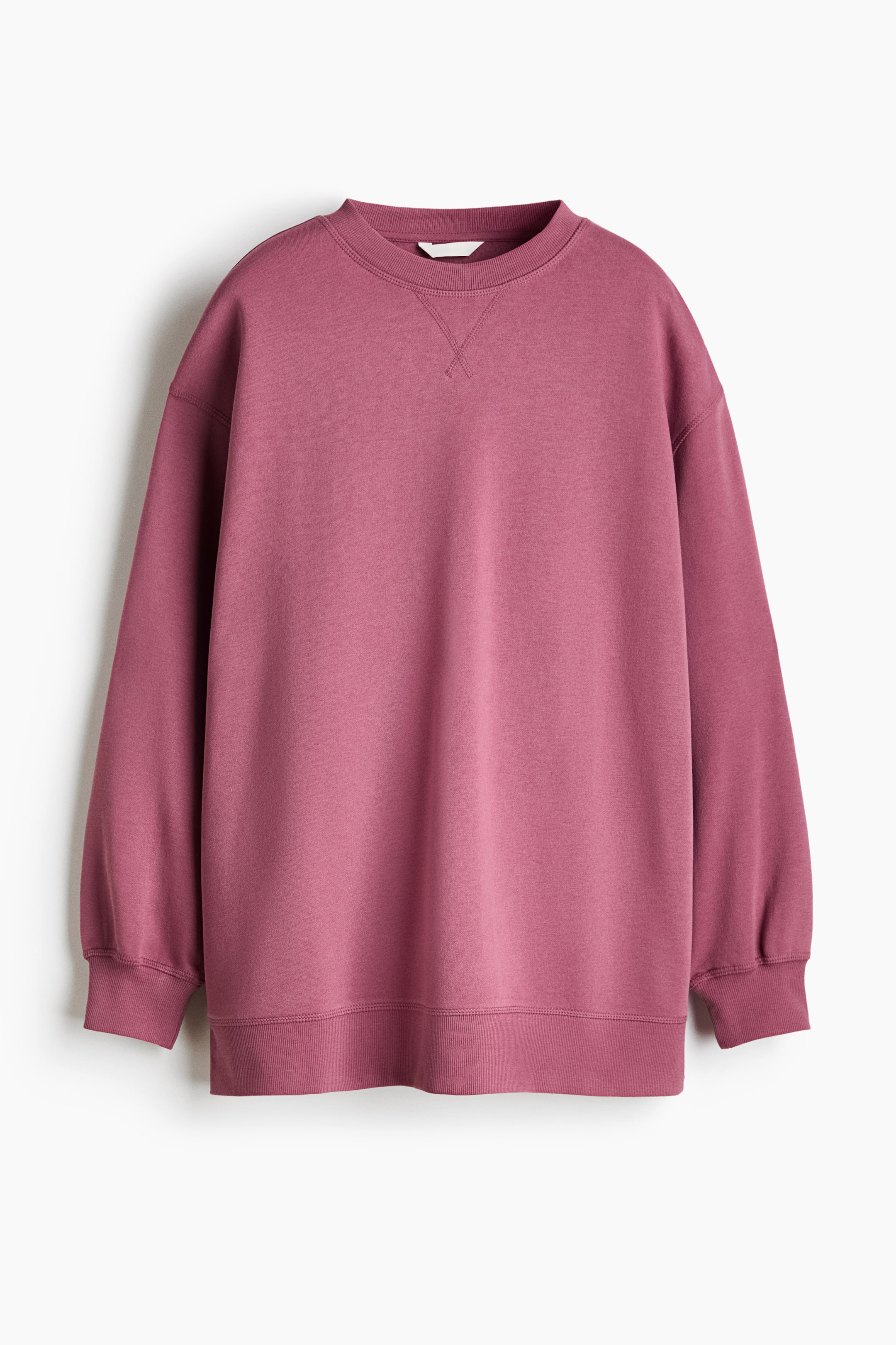 Προβολή μεγαλύτερης εικόνας: Ένα oversized φούτερ σε dusty rose απόχρωση παρουσιάζεται σε μπροστινή όψη, με χαμηλωμένους ώμους, μακριά μανίκια με ribbed μανσέτες και ribbed τελείωμα γύρω από τη στρογγυλή λαιμόκοψη και το στρίφωμα. Στο στήθος, ακριβώς κάτω από τον γιακά, διακρίνεται μια διακοσμητική λεπτομέρεια με ραφή σε σχήμα V.
