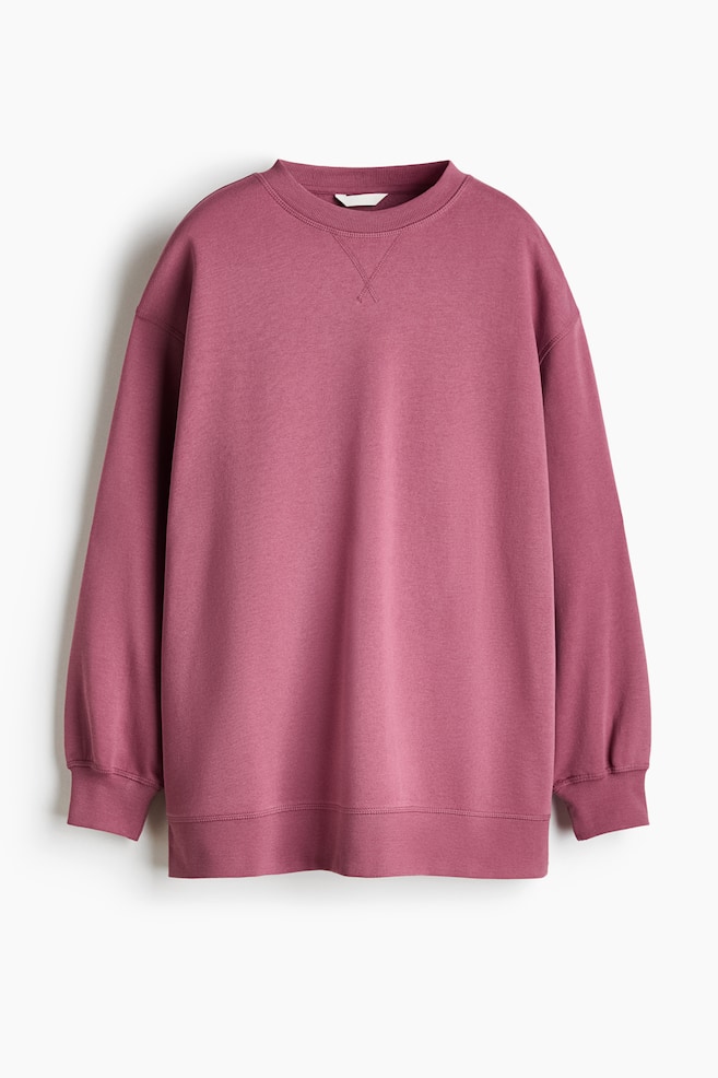 En oversized sweatshirt i stÃ¸vet rosa ses forfra og har sÃ¦nkede skuldre, lange Ã¦rmer med ribkanter ved manchetterne samt ribstrik ved den rundhalsede udskÃ¦ring og kanten forneden. En dekorativ V-syning er synlig pÃ¥ brystet lige under kraven. - 1