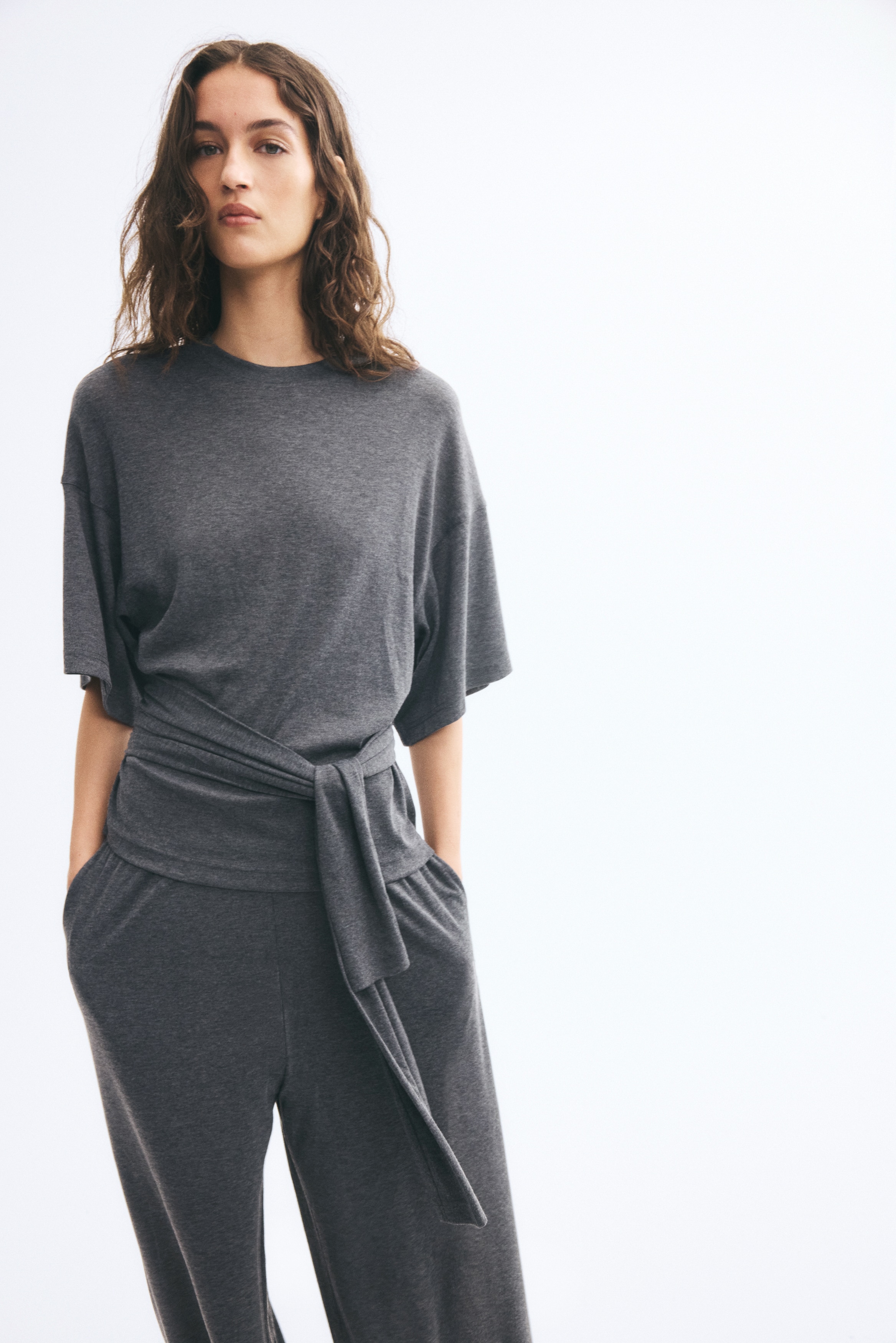 Má»t chiáº¿c Ã¡o jersey mÃ u xÃ¡m Äáº­m ÄÆ°á»£c chá»¥p á» gÃ³c nhÃ¬n chÃ­nh diá»n, cÃ³ cá» trÃ²n, vai rÆ¡i vÃ  tay Ã¡o rá»ng dÃ i Äáº¿n khuá»·u tay. Pháº§n Ã¡o ÄÆ°á»£c nháº¥n báº±ng nhá»¯ng dáº£i váº£i báº£n rá»ng buá»c nÃºt á» eo vÃ  buÃ´ng rá»§ xuá»ng phÃ­a trÆ°á»c.