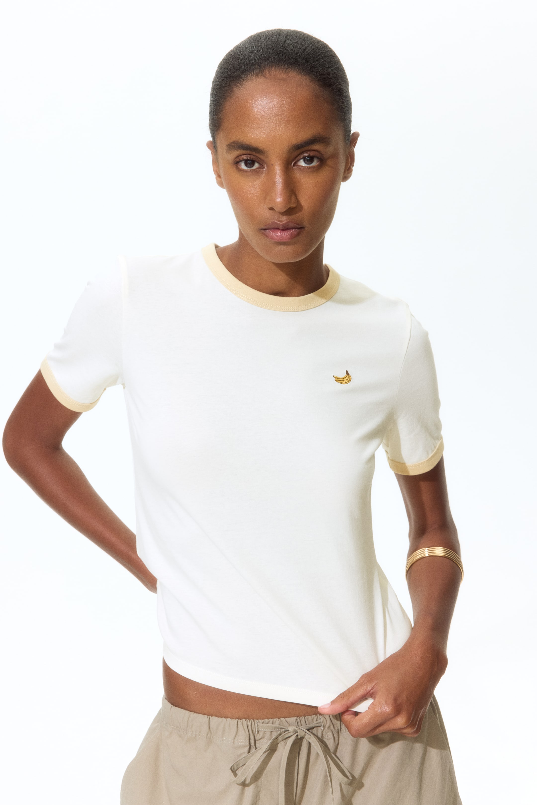View larger image: An off-white ringer t-shirt showcases a subtle light yellow trim on its crew neck and short sleeve cuffs. A small embroidered banana is prominently visible on the left chest, and the t-shirt is displayed facing forward.