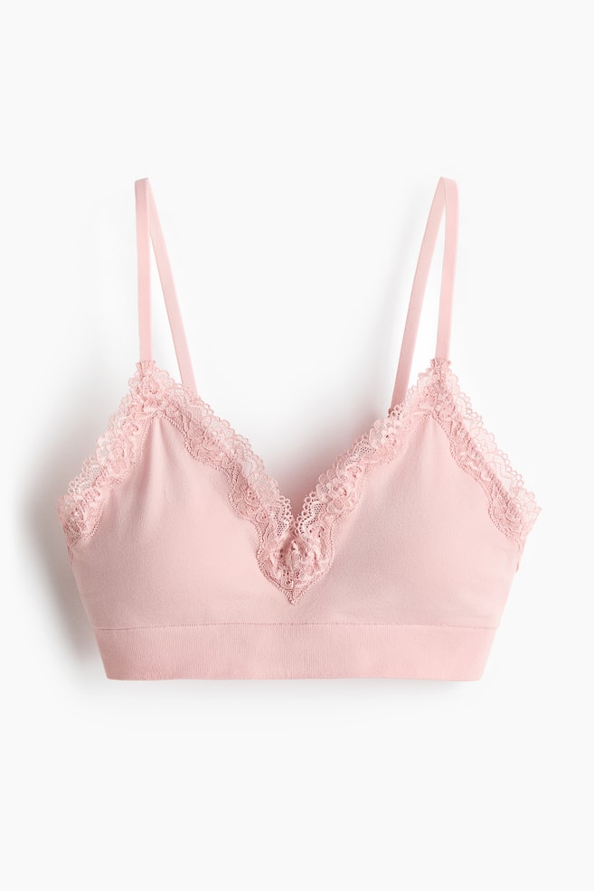 Soft pink bra shown from the front, featuring adjustable shoulder straps, smooth cups with delicate lace trim along the top edges forming a V-shape at the centre front, and a wide band beneath the cups. - 1