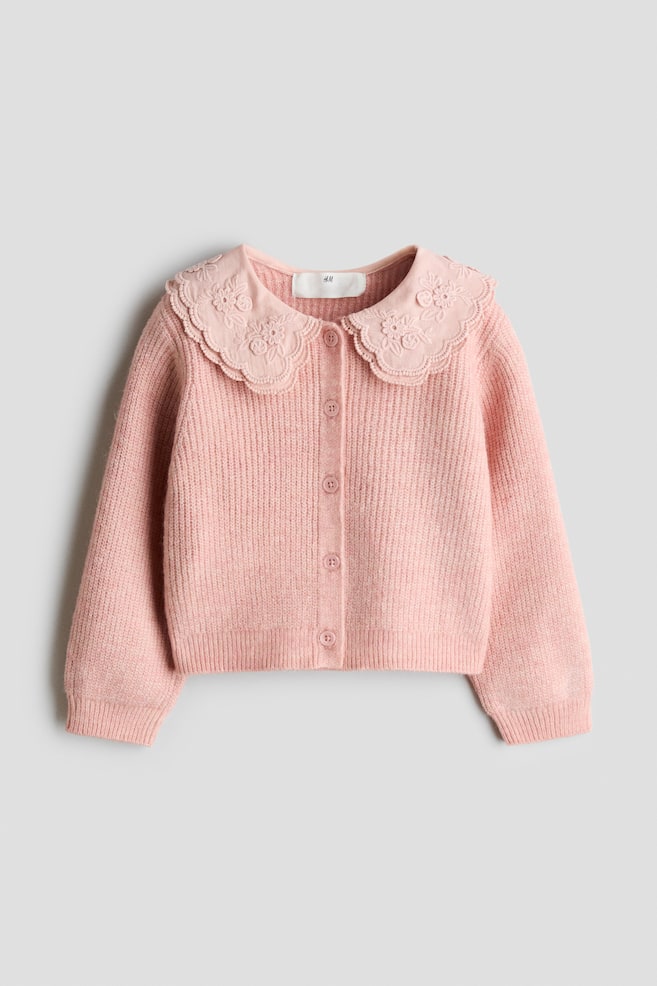 A pink knitted cardigan is facing forwards, displaying a ribbed texture and a button-up fastening with matching pink buttons. It features a wide, scalloped Peter Pan collar with embroidered floral details, along with ribbed cuffs and a ribbed hem. - 1