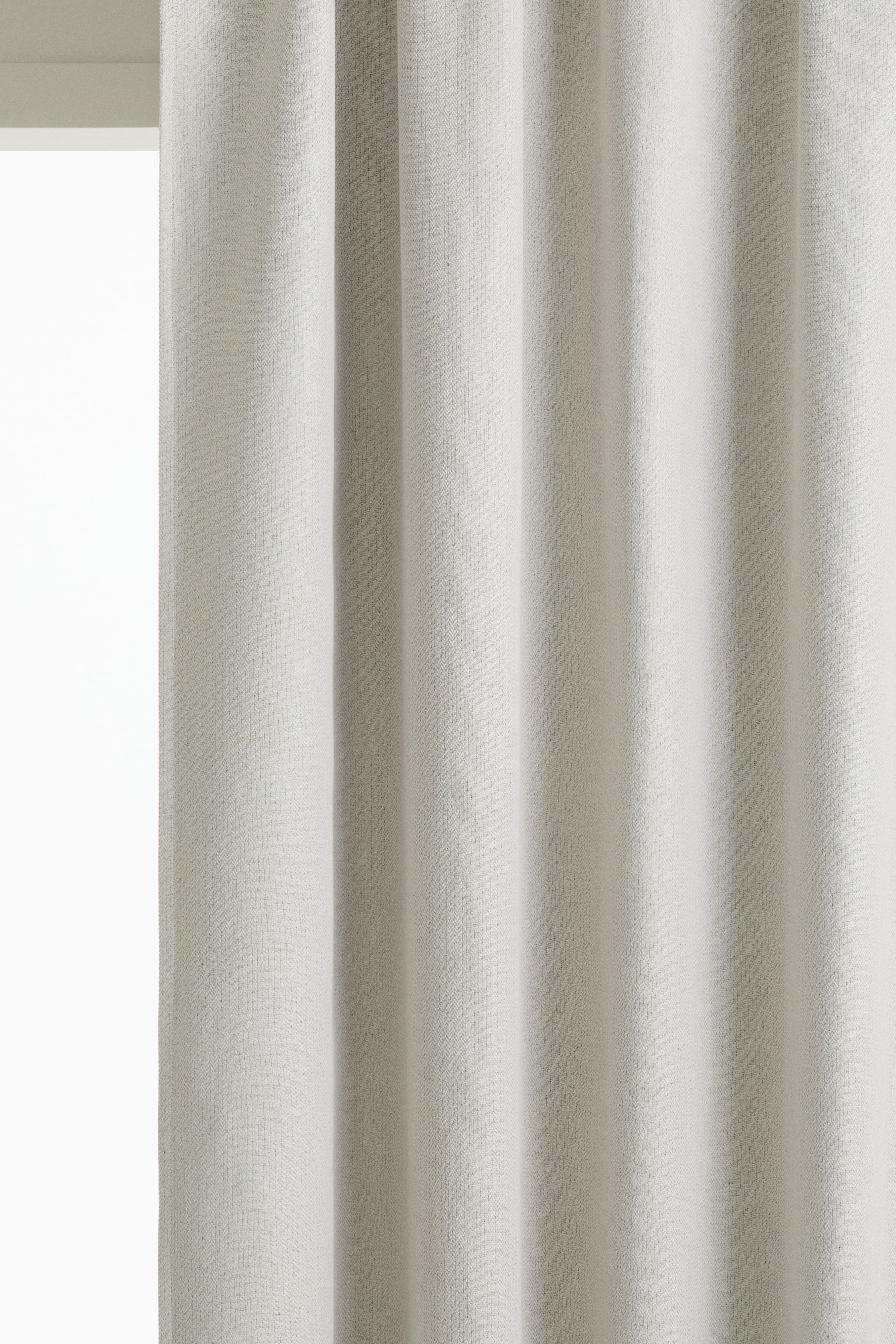 View larger image: A light off-white curtain panel is shown from the front, featuring a dense herringbone weave and hanging in soft vertical folds.