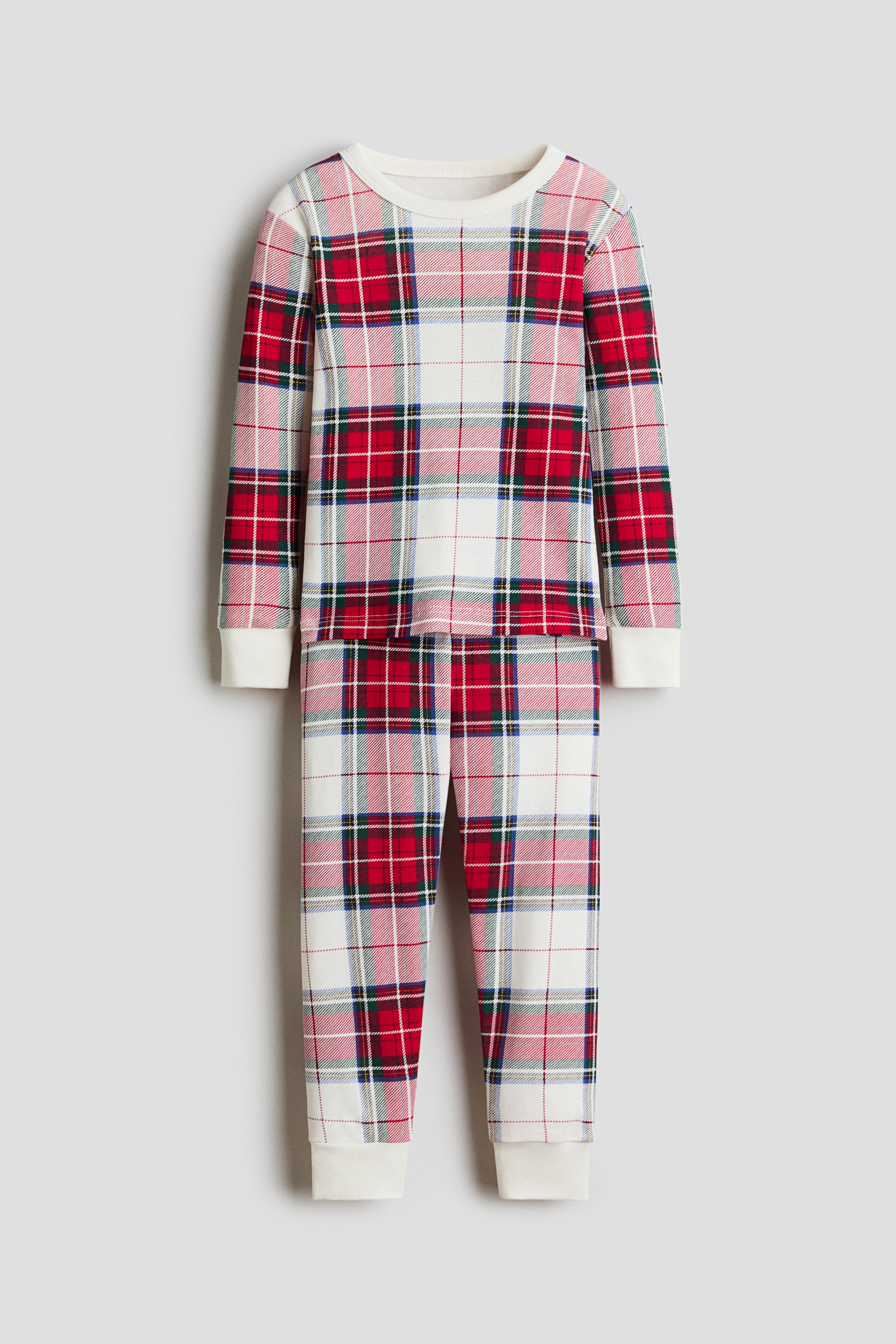 View larger image: A two-piece pajama set is shown with a matching long-sleeved shirt and pants in a red, green, and white plaid pattern, facing front. The shirt features a narrow-trimmed crew neck and white ribbed cuffs, while the pants end in matching white ribbed hems.