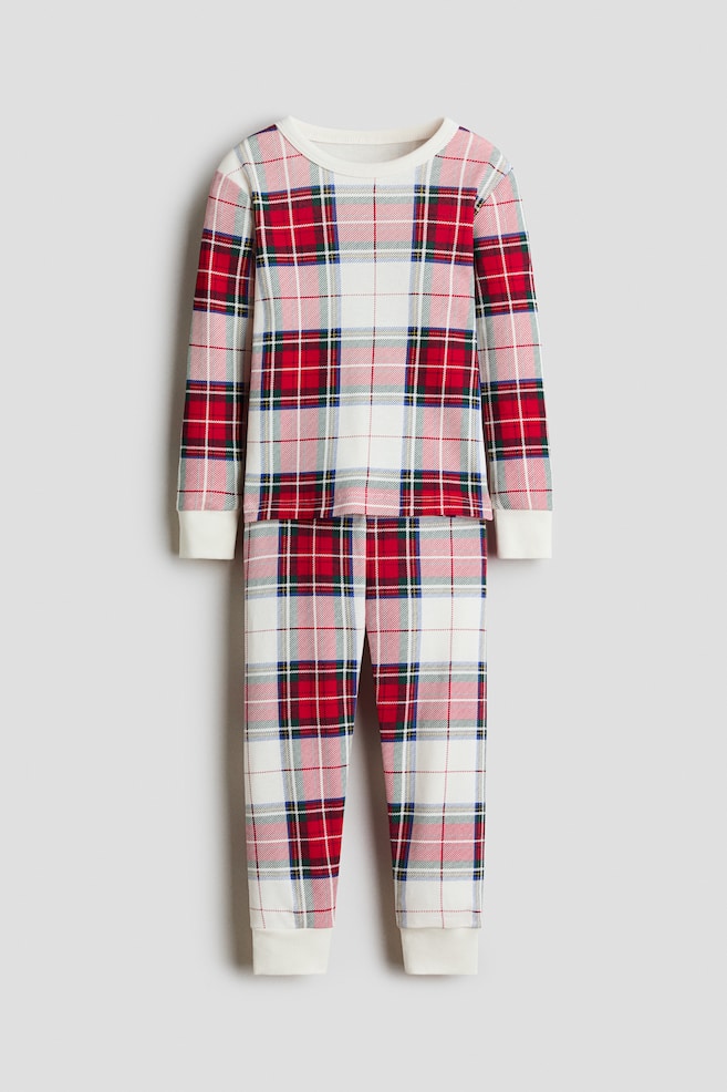 A two-piece pajama set is showing a matching long-sleeved shirt and pants in a red, green, and white plaid pattern, facing front. The shirt is featuring a narrow-trimmed round neck and white ribbed cuffs, while the pants are ending in matching white ribbed hems. - 1