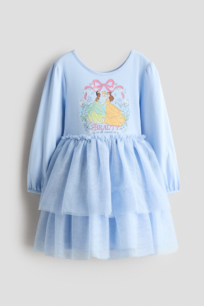 A light blue long-sleeve dress is facing front, featuring a scoop neckline and a chest graphic depicting Disney princesses beneath a pink bow and the text "BEAUTY is all around us." The dress is styled with elasticized cuffs and a tiered, ruffled tulle skirt covered in fine glitter. - 1