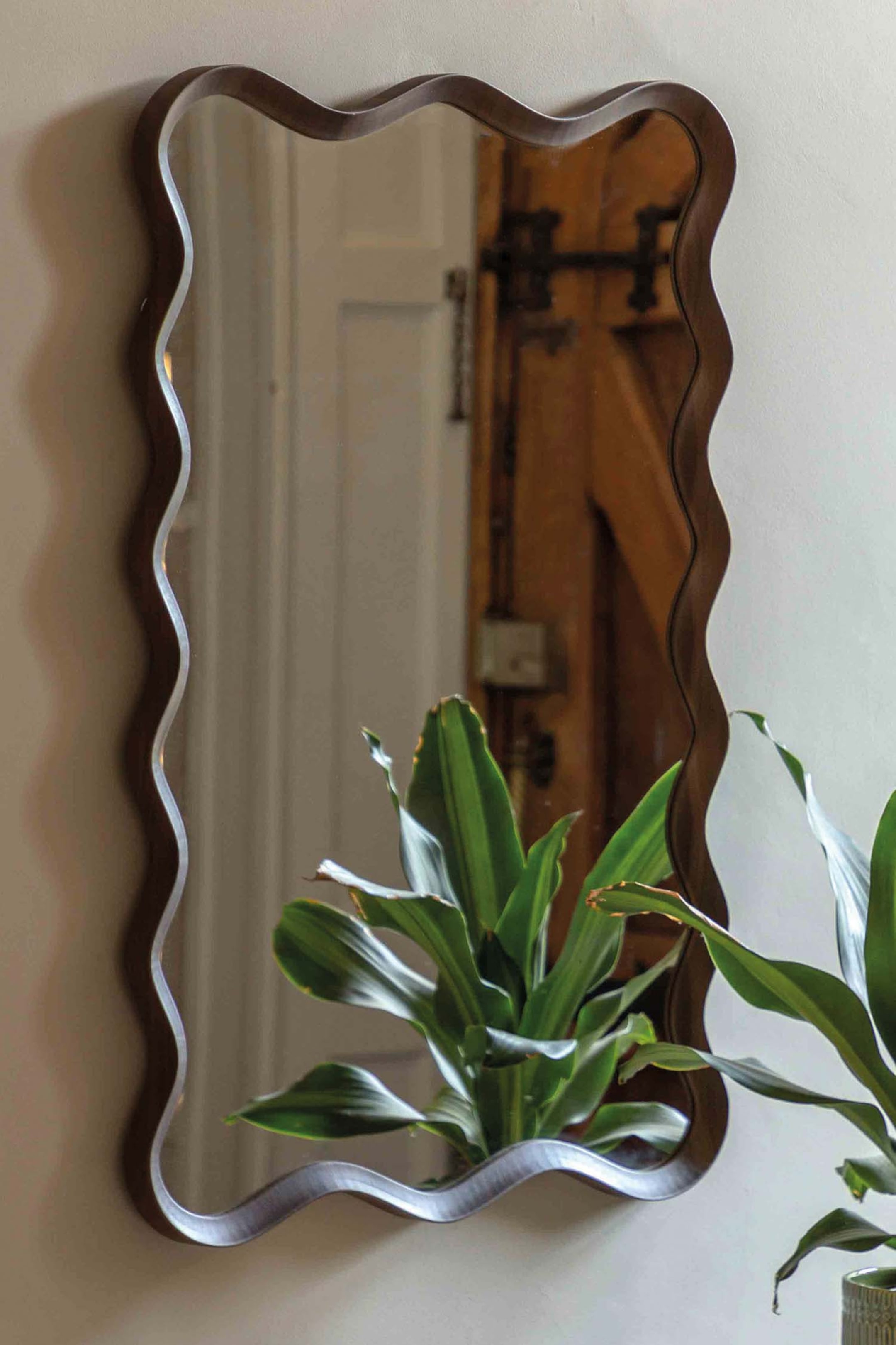 View larger image: A mirror featuring a dark brown frame with an irregular, wavy outline. It is displayed vertically.