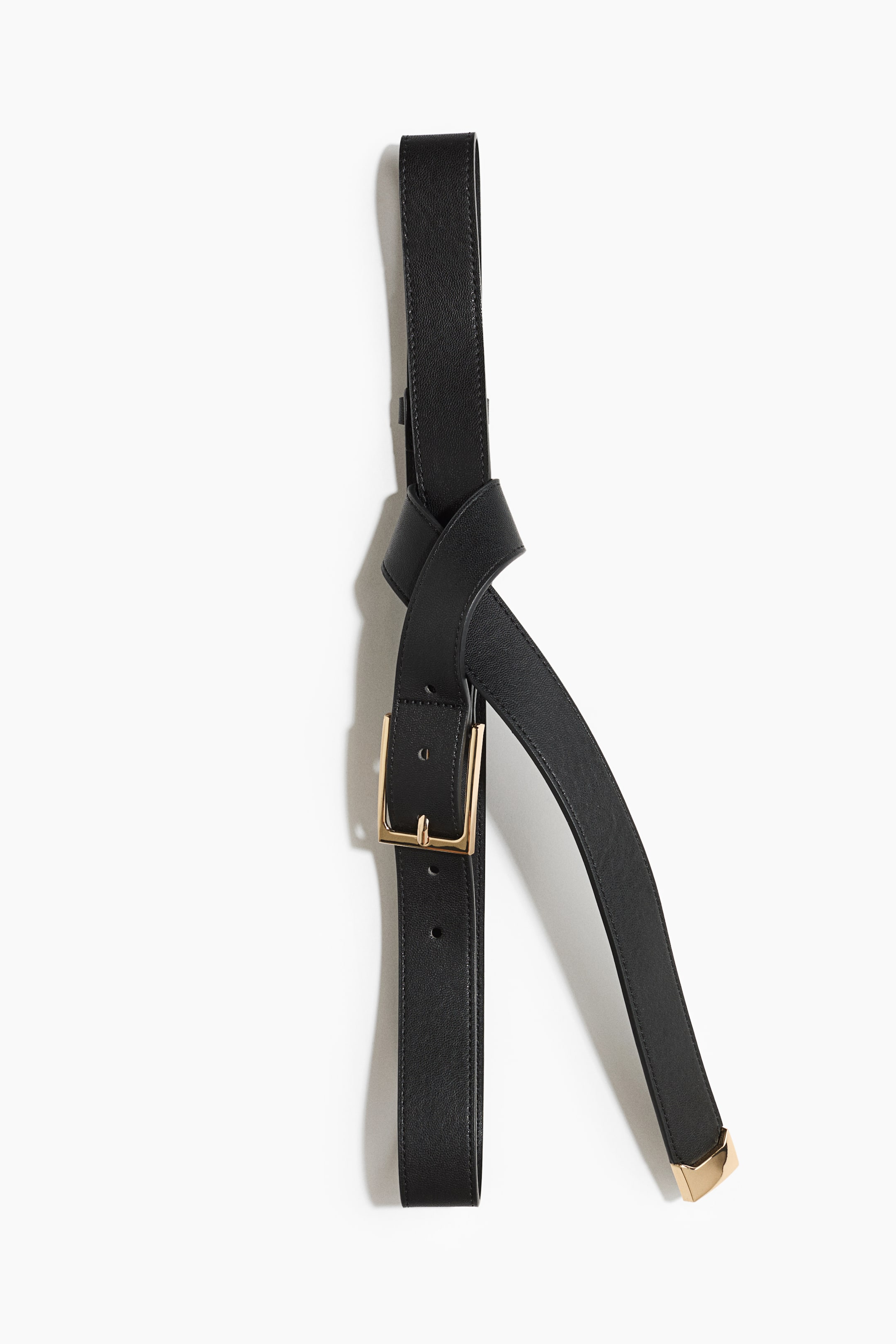 View larger image: A black leather belt is hanging vertically, showing its front side with a loose knot tied at the center. The belt features a textured finish, a gold-tone rectangular buckle on one hanging end, and a matching gold-tone metal tip on the other curved end.