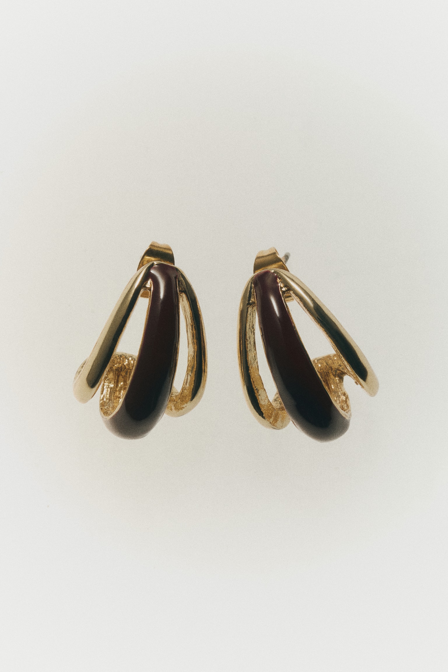 A pair of drop-shaped earrings is displaying a layered, curved design from a front-facing view. The earrings are combining polished gold-toned metal loops with a central, glossy dark brown plastic inlay. - 1
