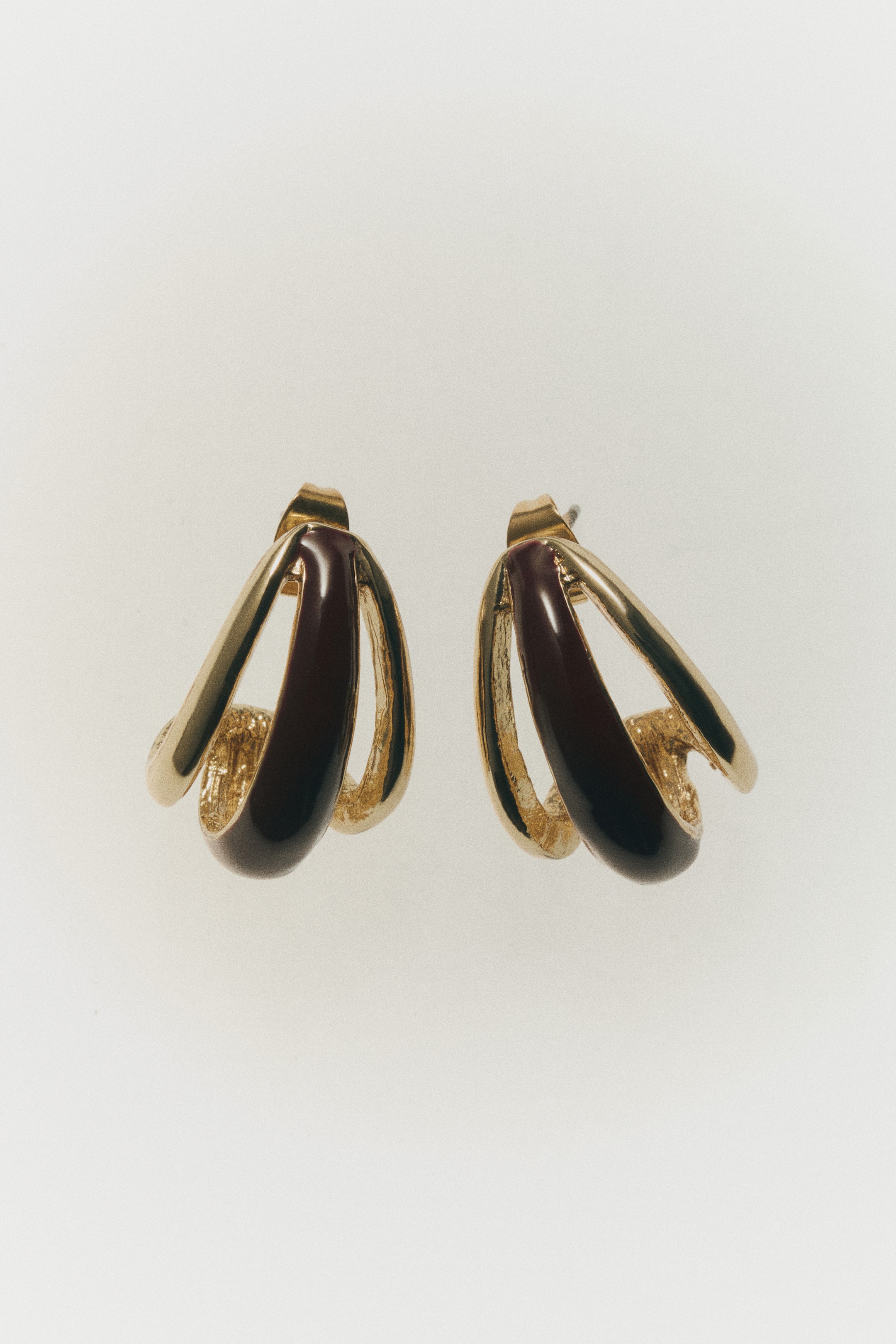 View larger image: A pair of teardrop earrings is displayed in a front-facing view, showing a layered, curved design. The earrings combine polished gold-toned metal loops with a central glossy dark brown plastic inlay.