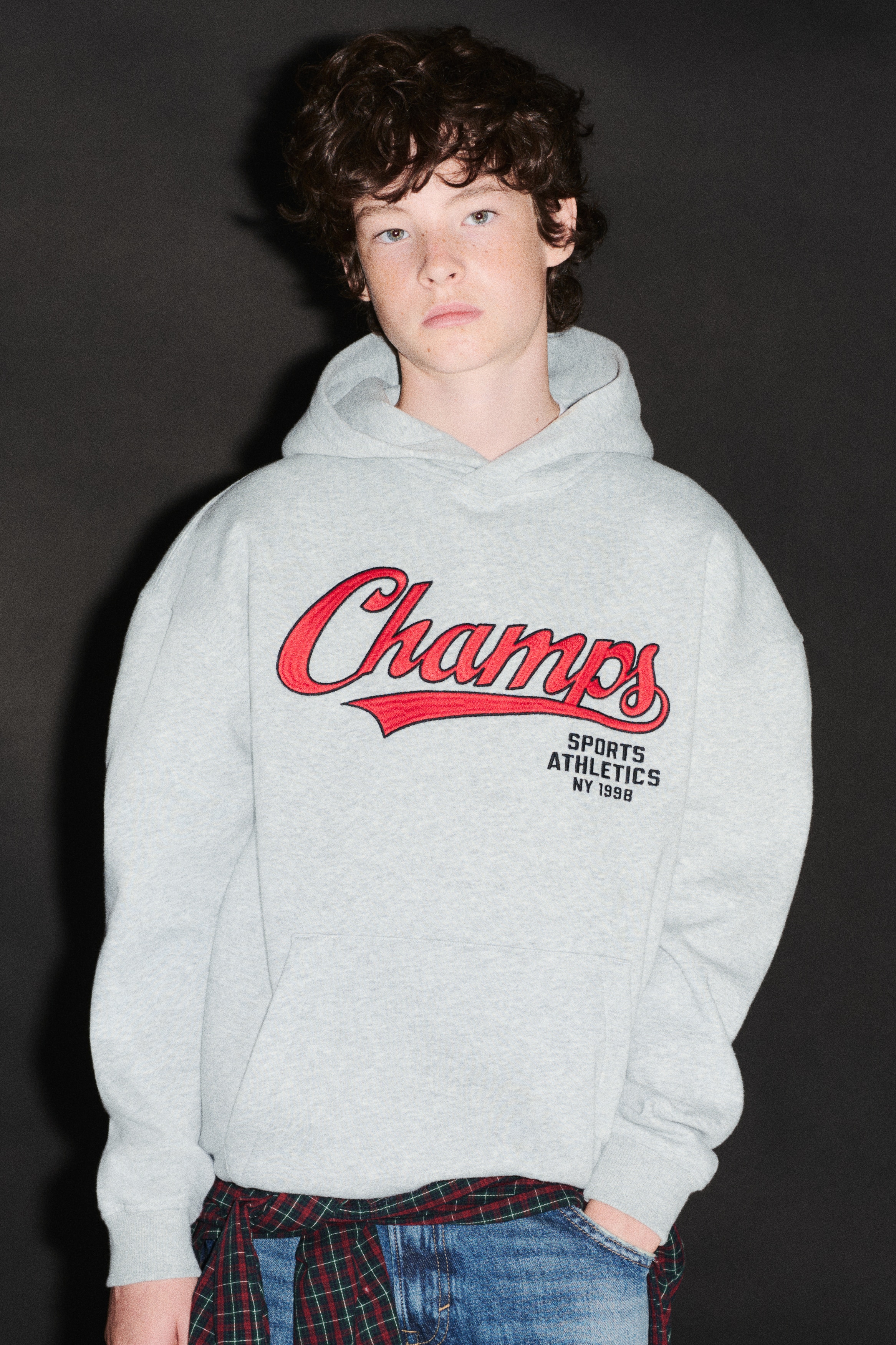 ä¸ä»¶æ·ºç°è²æ··ç´¡é£å¸½ä¸è¡£ä»¥åè¦è§å±ç¤ºï¼è¸åé£¾æç´è²æå¯«é«ãChampsãåæ¡ï¼ä¸¦æ­éé»è²æå­ãSPORTS ATHLETICS NY 1998ããéæ¬¾å¯¬é¬çåæé£¾åç¾è½è©è¨­è¨ãåè¥äº¤çå¼é£å¸½ãè¢é¼ å£è¢ï¼ä»¥åè¢å£åä¸æºçç¾ç´æ¶éã