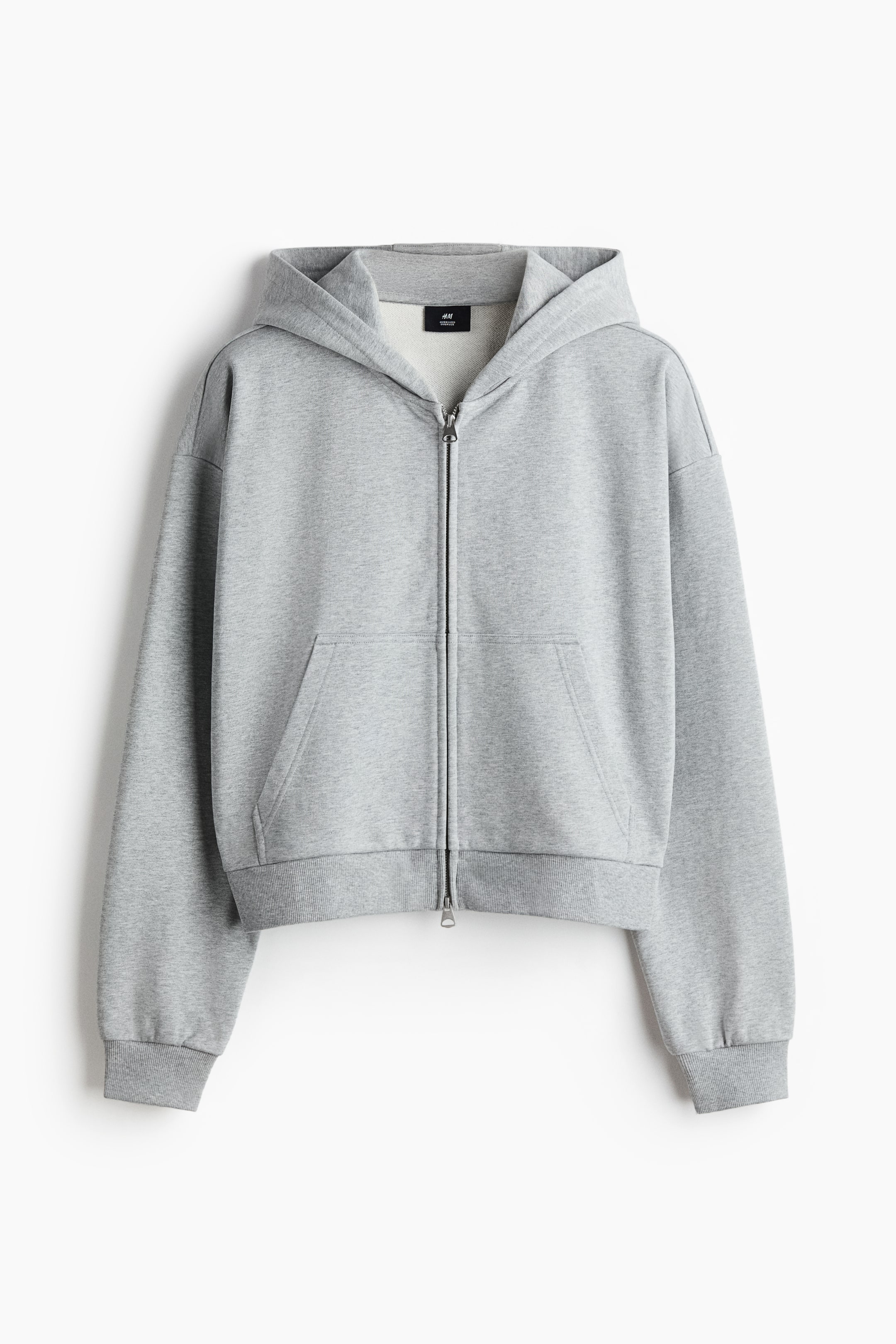 View larger image: A gray short zip-through hoodie in sweatshirt fabric is facing FRONT, showcasing an oversized fit with dropped shoulders and long sleeves. It features a jersey-lined hood, a two-way zipper closure down the front, front kangaroo pockets, and wide ribbed trims at the cuffs and hem.