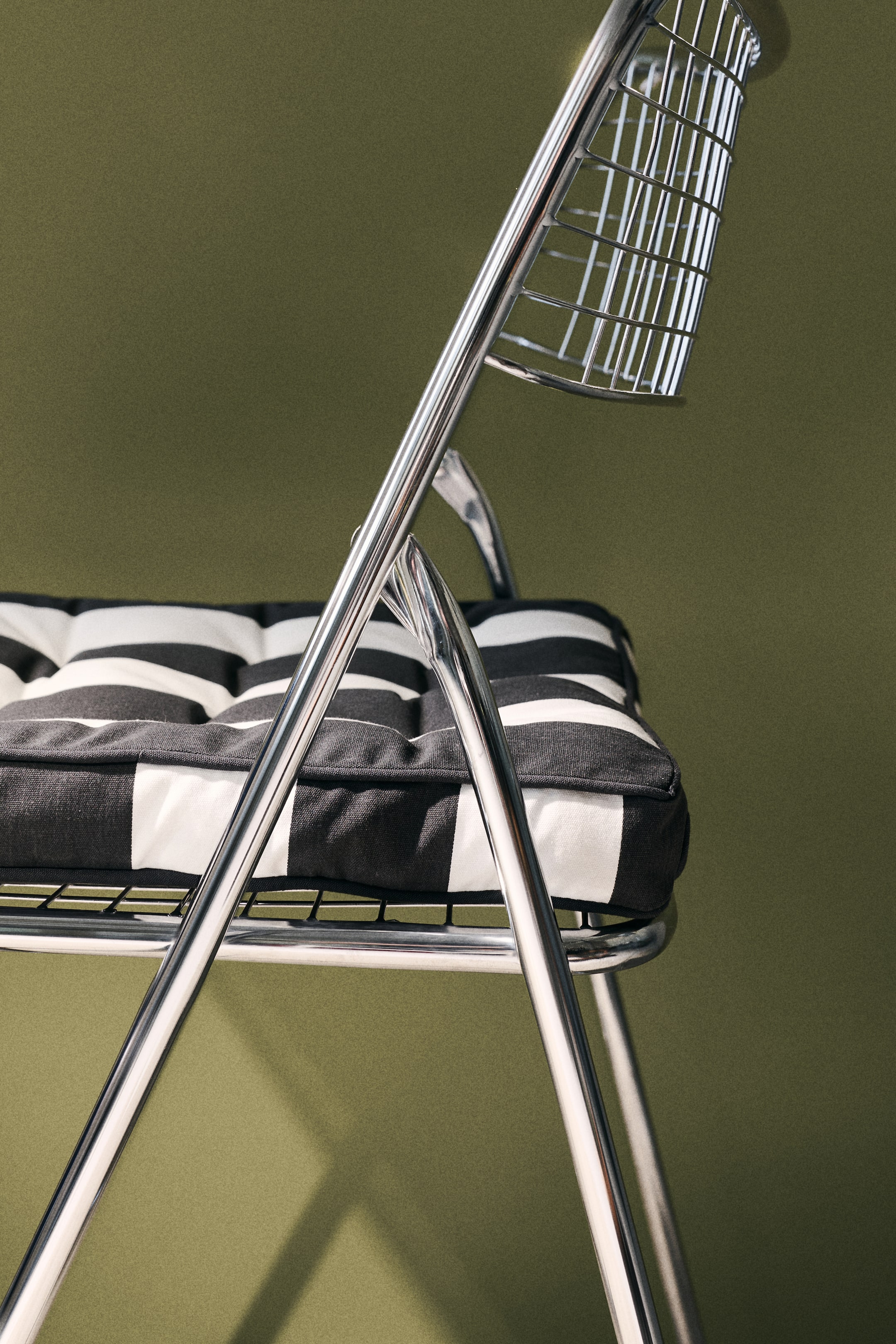 View larger image: A cushioned seat pad is perched on a metal chair, viewed from a side-front perspective. It boasts a timeless black and white striped design, complete with piping along the edges and quilted knots adorning its surface.