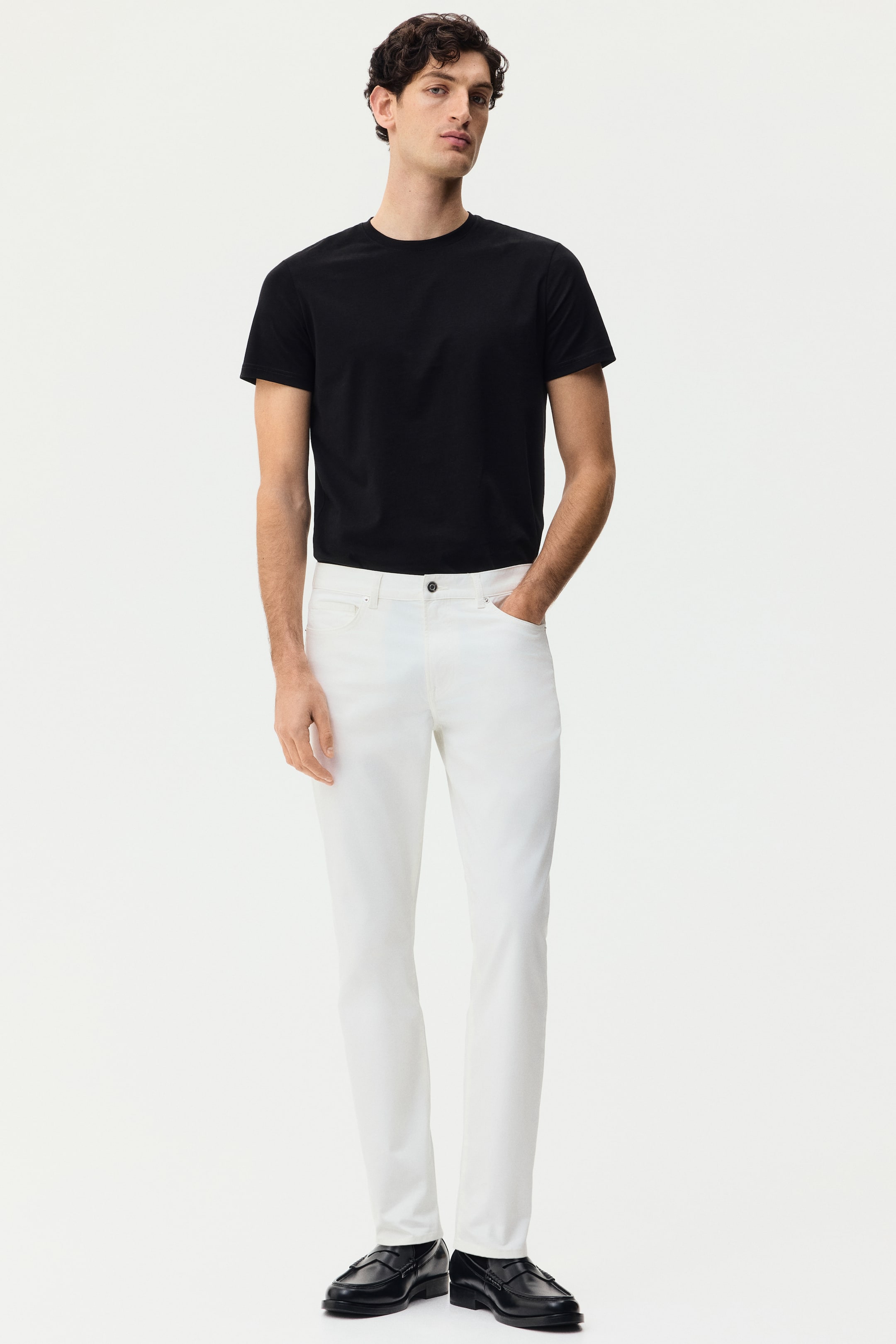 View larger image: A black short-sleeve t-shirt is featuring a crew neck and a plain design, paired with white slim-fit trousers that are showing front pockets and a button closure. Black slip-on loafers are completing the ensemble.