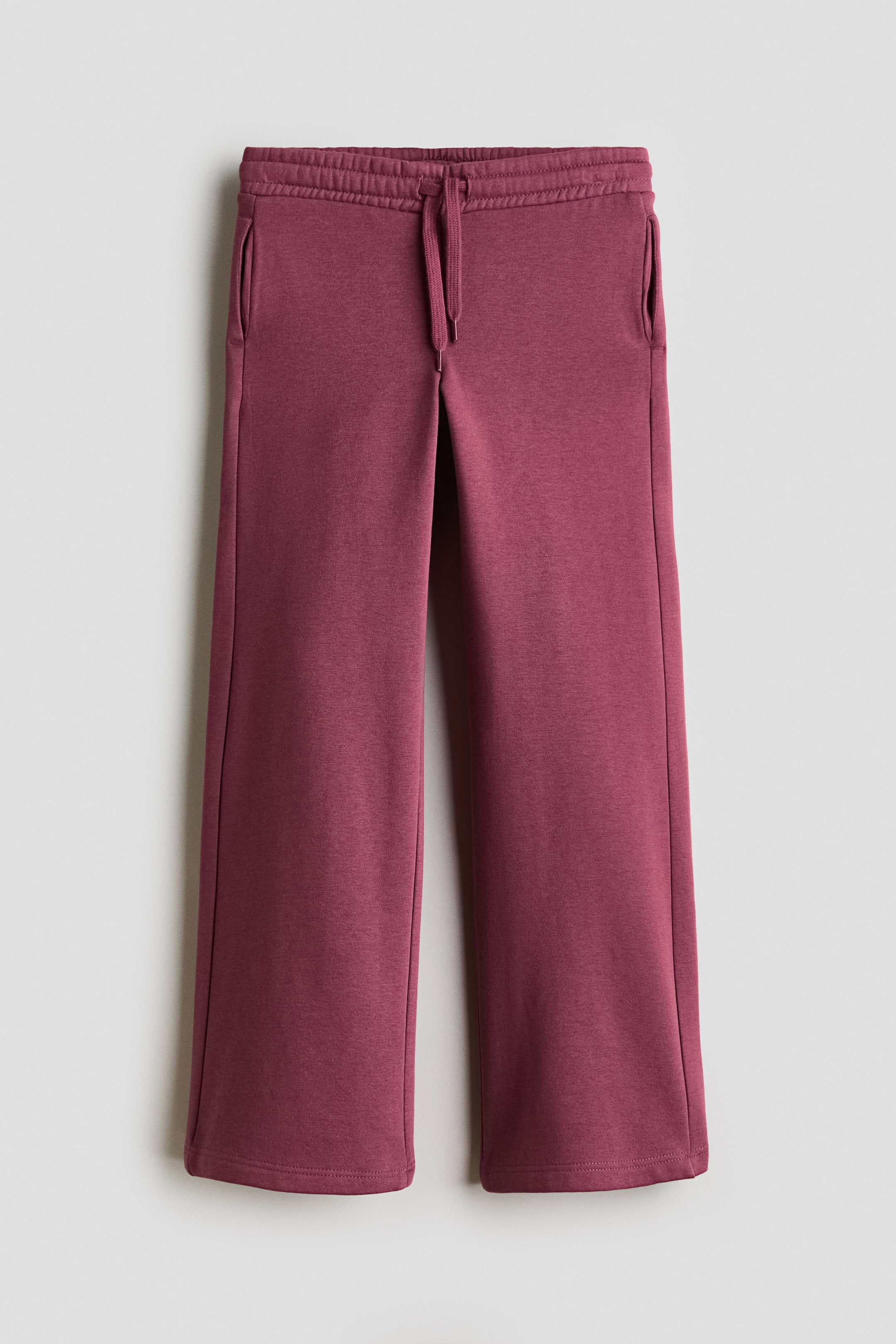View larger image: A pair of dark pink track pants is shown from the front, featuring an elastic waistband with a matching drawstring and discreet side pockets. The pants fall into straight legs with clean-finished hems.