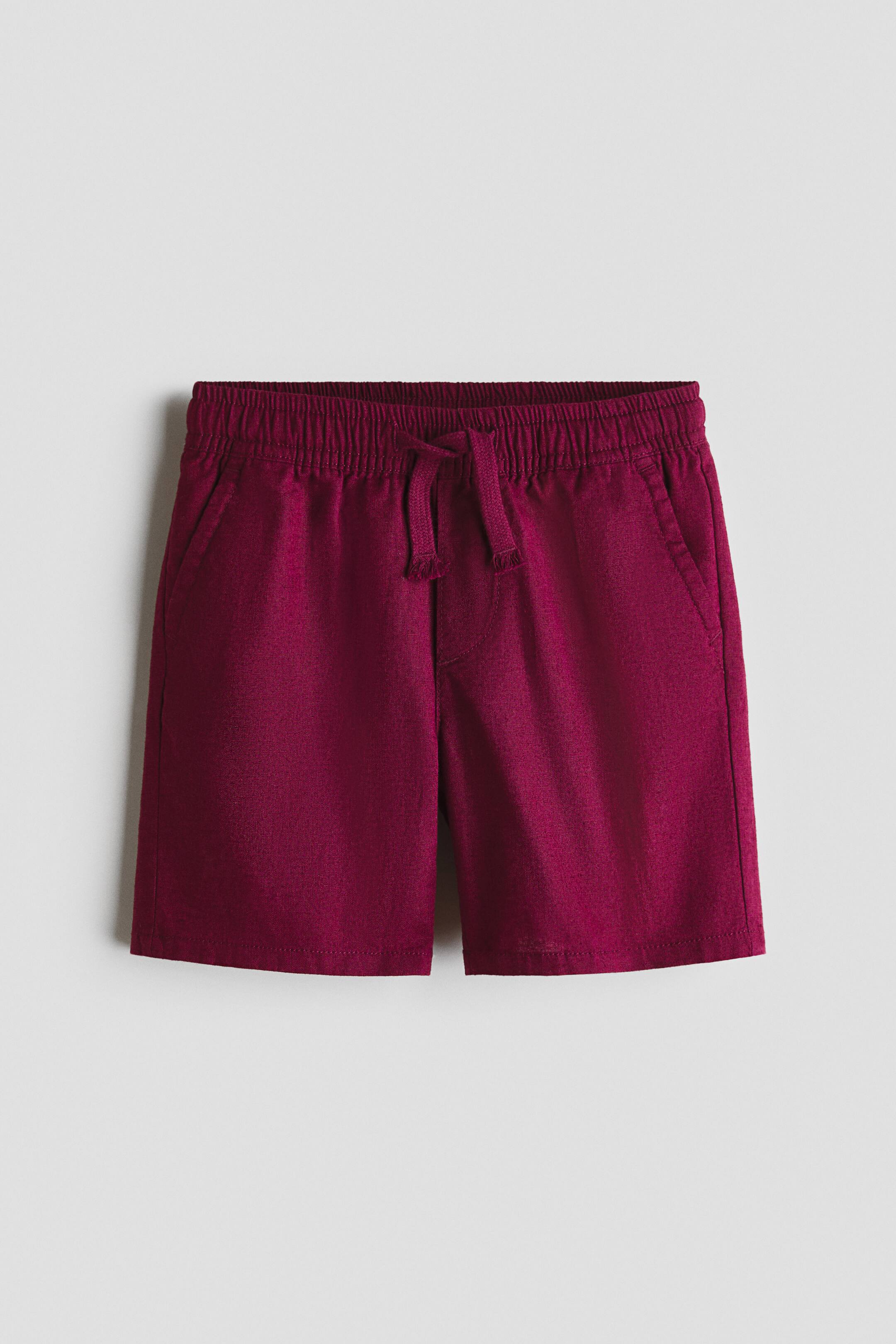 View larger image: The burgundy shorts feature an elastic waistband with a drawstring tied at the front. Two slash pockets are visible on the sides of the textured fabric.