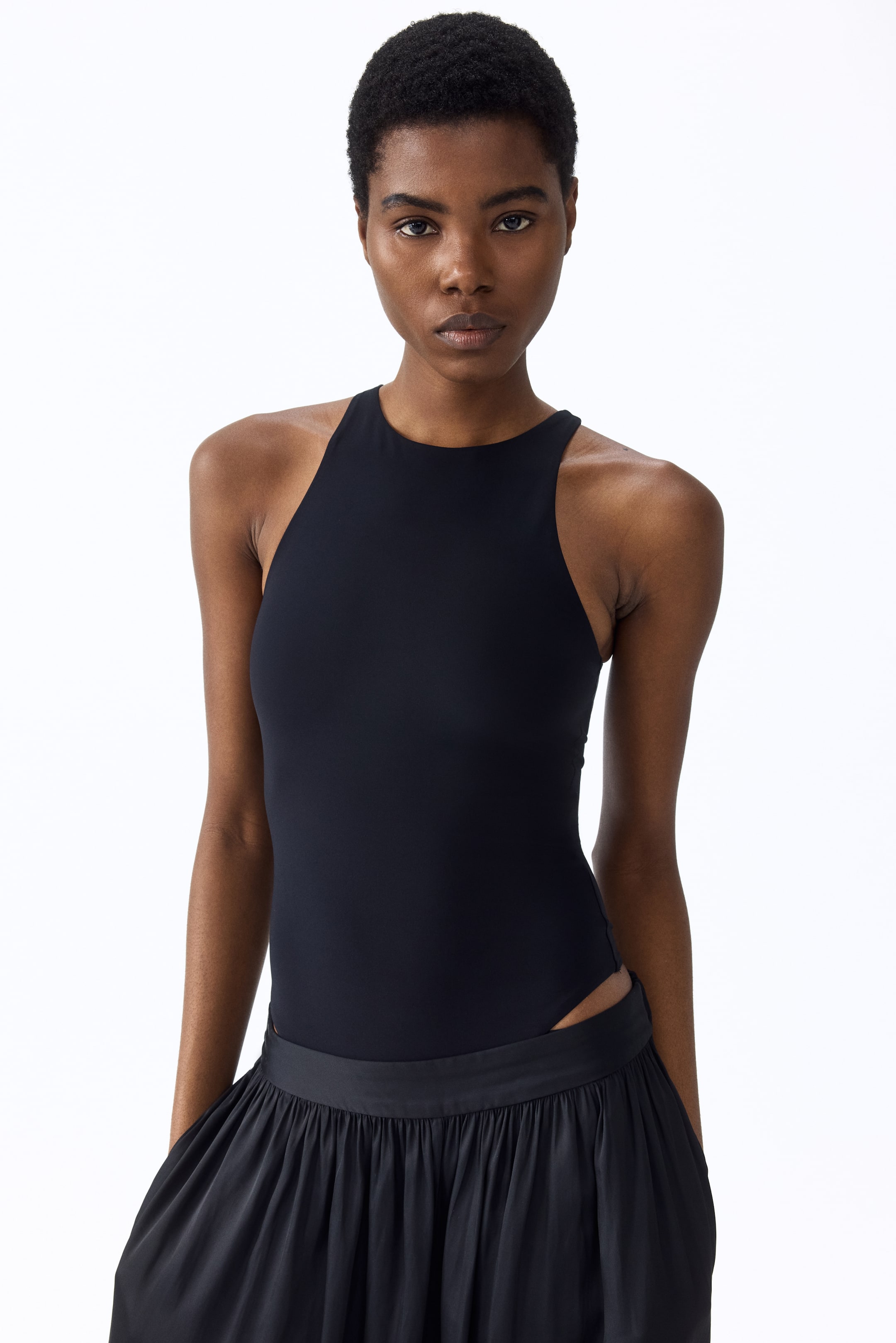 View larger image: A black high-neck bodysuit featuring a sleeveless racerback design and a snug fit, with a high-cut leg opening visible at the hip.