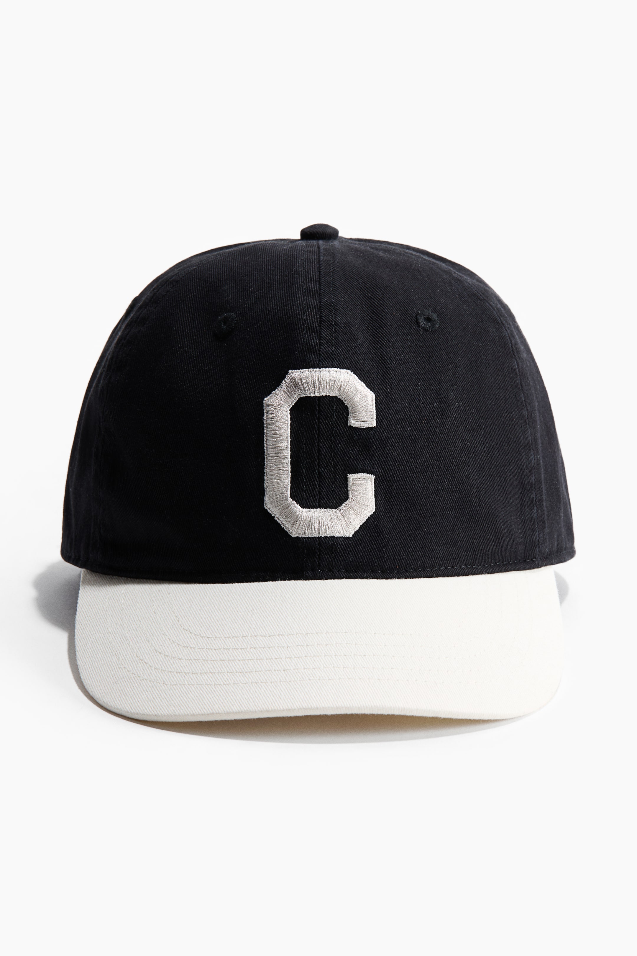 Ver imagen más grande: Una gorra se presenta de FRENTE, con una corona de sarga de algodón negro y una letra "C" bordada en gris claro en la parte frontal. Cuenta con una visera blanca en contraste y ojales bordados en la corona.