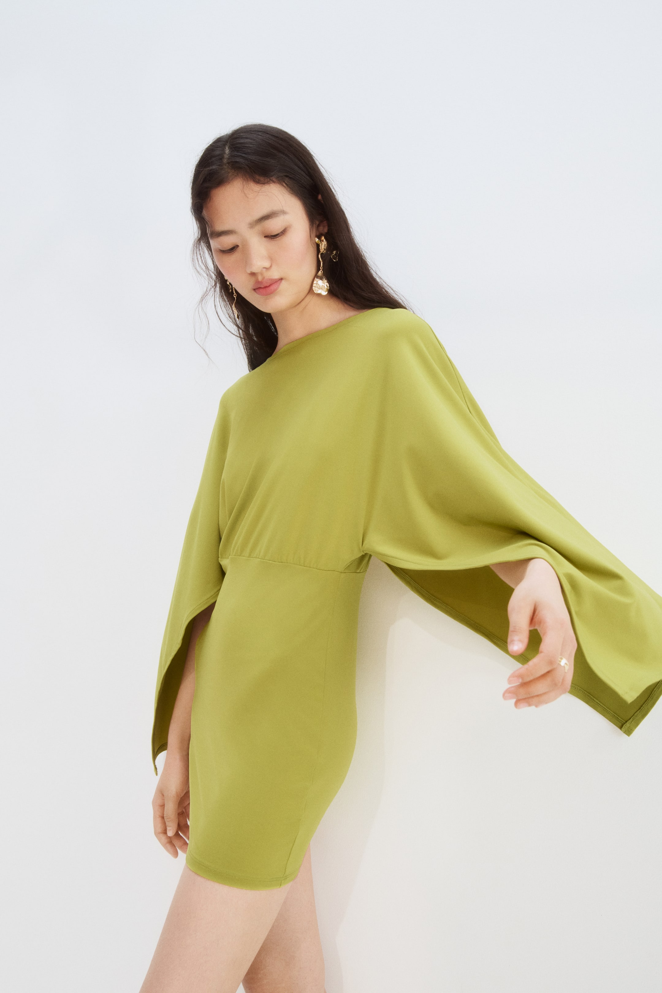 View larger image: This chartreuse mini dress features a round neckline and wide, flowing batwing sleeves that create an open, cape-like effect. It showcases a cinched waistline and a fitted short skirt.