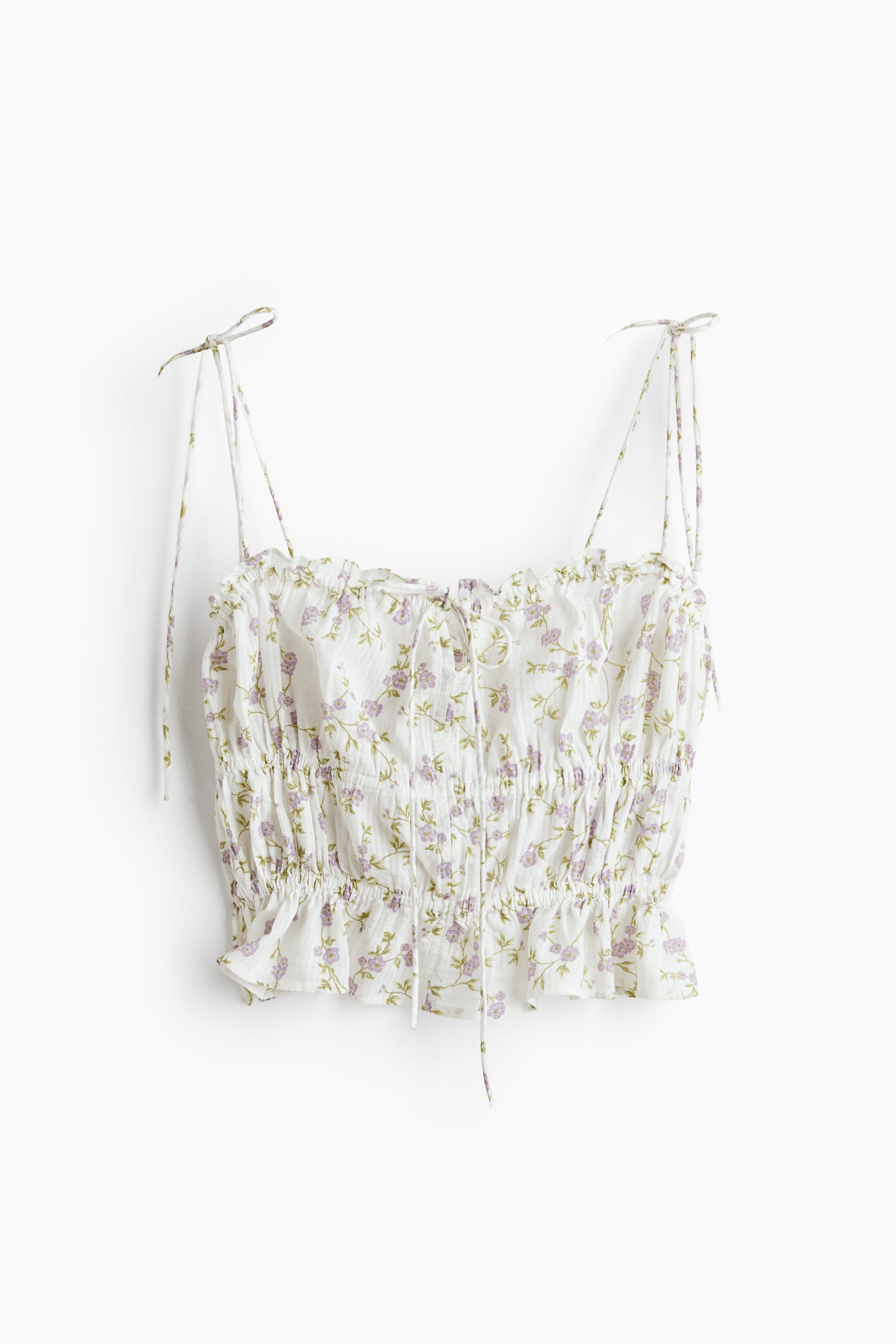 Xem ảnh lớn hơn: Áo crop top màu trắng có kết cấu nhăn nhẹ và họa tiết hoa nhỏ màu tím và xanh lá. Thiết kế với dây buộc spaghetti, cổ vuông xếp nếp với dây buộc ở trung tâm phía trước, và phần thân áo xếp ly kết thúc bằng viền xếp nếp.