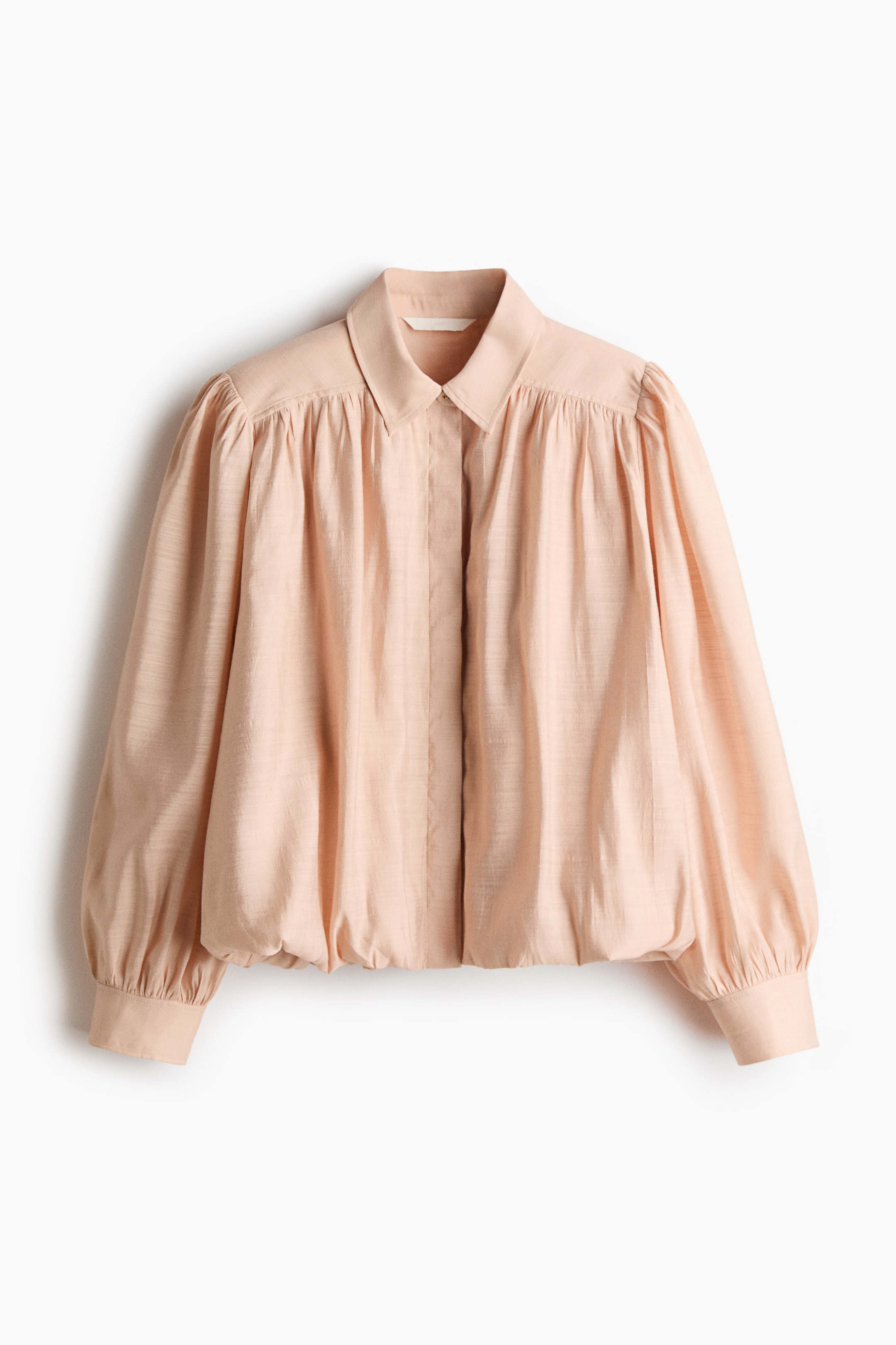 View larger image: A cropped jacket in a light peach-coloured woven fabric is shown facing front, featuring a pointed collar, a concealed front button placket, and heavy gathering at the shoulders. The jacket features voluminous puff sleeves with wide cuffs and a gathered bubble hem that creates a puffy, cropped silhouette.