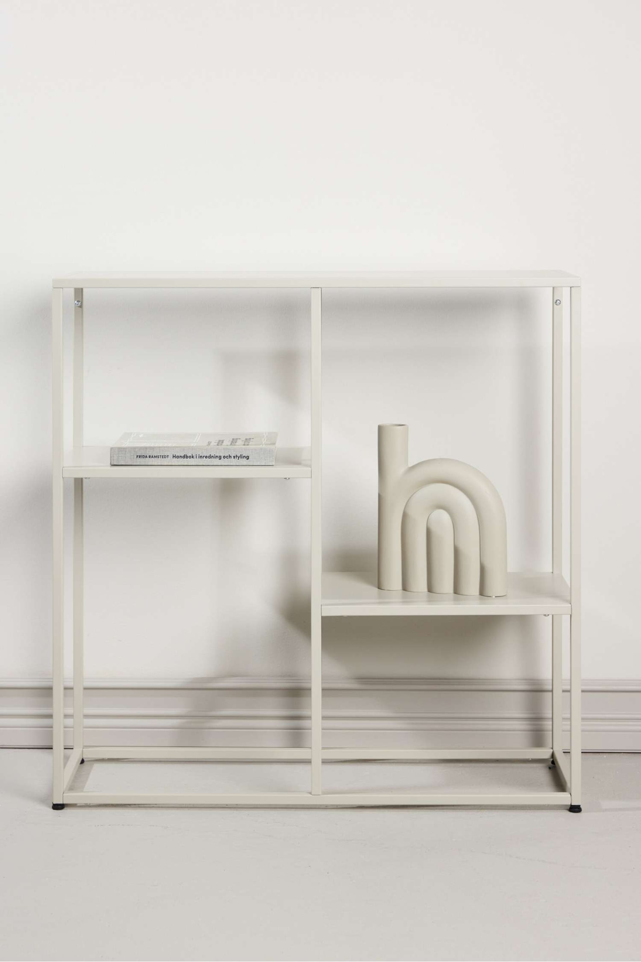 Agrandir l'image: L'étagère ouverte de couleur beige clair est orientée directement vers l'avant, avec un cadre métallique rectangulaire carré doté de plusieurs étagères horizontales. L'unité expose un livre sur l'étagère supérieure gauche et un vase décoratif sur l'étagère du milieu à droite, mettant en valeur sa capacité de rangement à travers ses deux sections verticales principales.