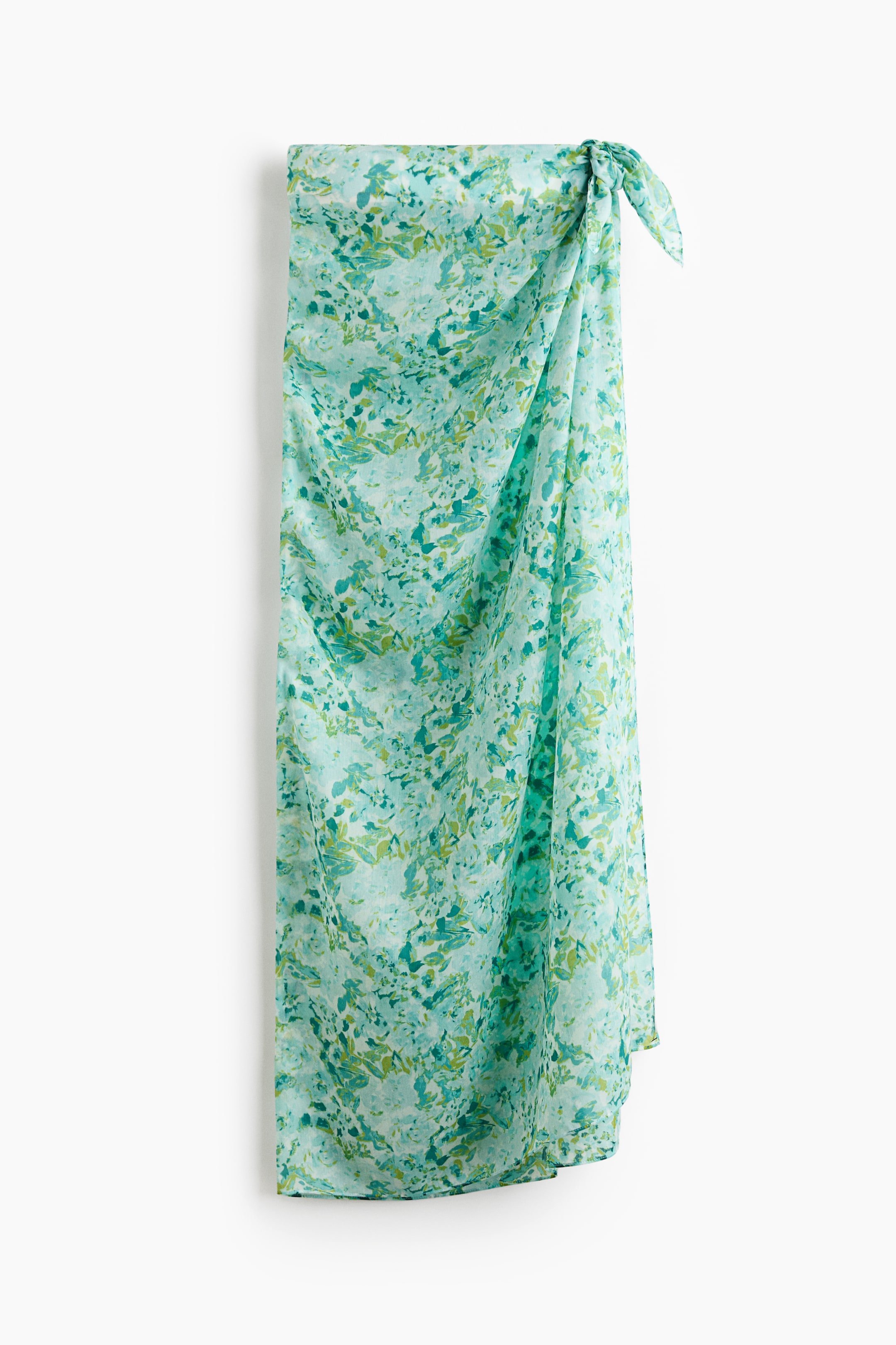Grotere afbeelding bekijken: Een lange sarong in luchtige voile toont een groen en blauw gevlekt patroon en wordt aan de voorkant vastgeknoopt, waardoor een rok ontstaat.