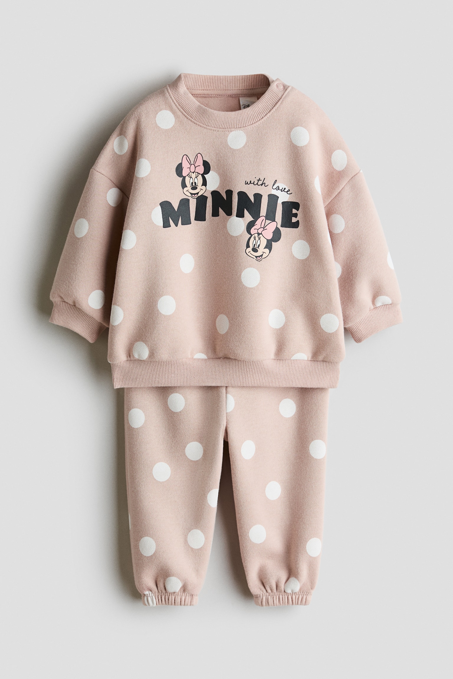Má»t bá» Äá» ná» in 2 mÃ³n mÃ u há»ng nháº¡t vá»i há»a tiáº¿t cháº¥m bi tráº¯ng ÄÆ°á»£c chá»¥p á» máº·t trÆ°á»c, gá»m Ã¡o sweatshirt tay dÃ i vÃ  quáº§n sweatpants Äá»ng bá». Ão sweatshirt ná»i báº­t vá»i hÃ¬nh Minnie Mouse vÃ  dÃ²ng chá»¯ âMINNIEâ trÃªn ngá»±c, cÃ¹ng cá» trÃ²n bo gÃ¢n, bo tay bo gÃ¢n vÃ  gáº¥u Ã¡o bo gÃ¢n, trong khi quáº§n sweatpants cÃ³ pháº§n á»ng bo chun nhÃºn á» gáº¥u.