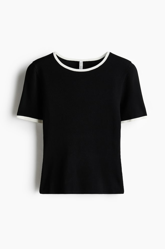 The front of a black fine-knit short-sleeved top is displaying a round neckline and short sleeves, both edged with white trim. - 1