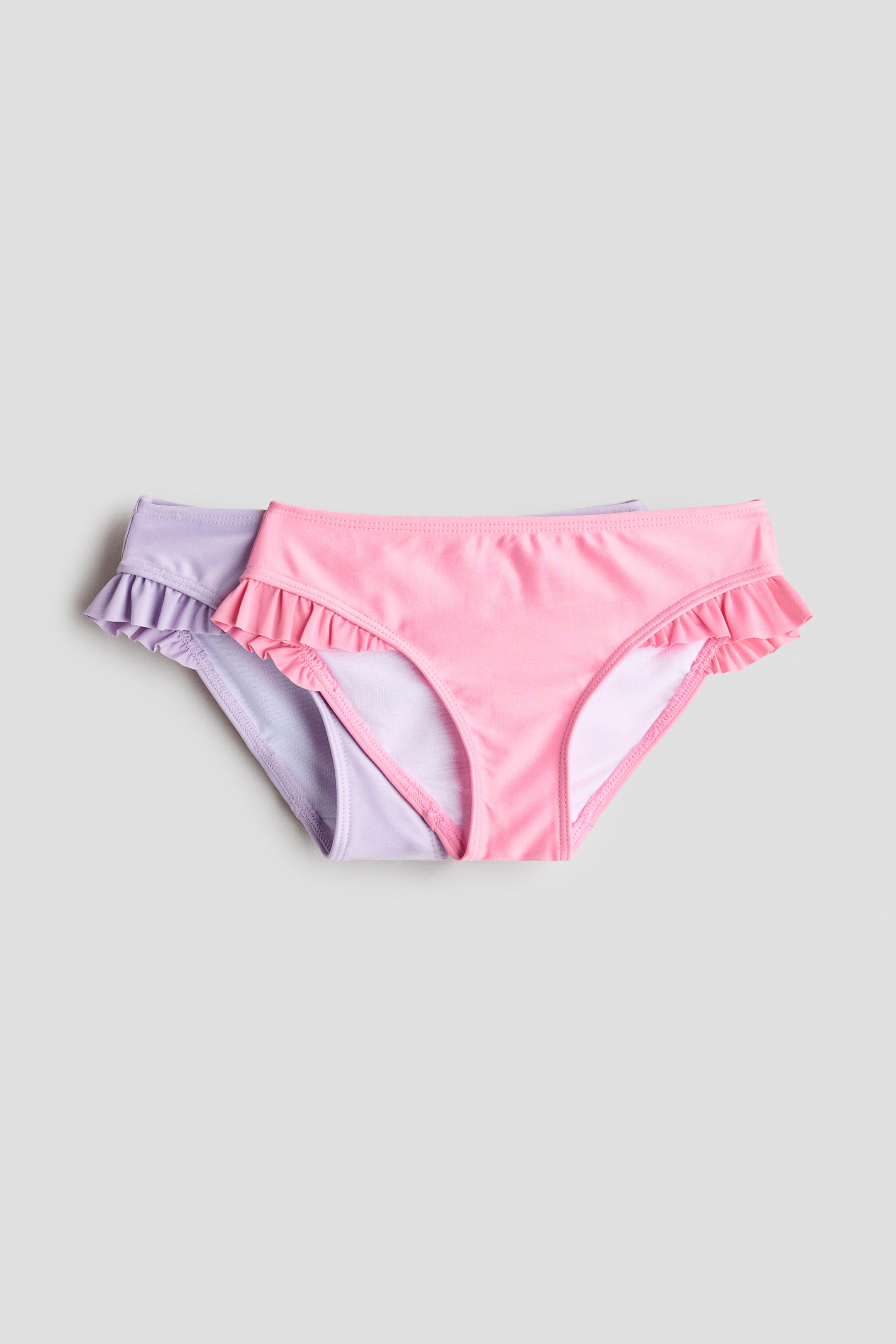 Ingrandisci l'immagine: Due slip bikini completamente foderati sono esposti frontalmente, uno in rosa e uno in lavanda. Entrambi presentano un bordo arricciato ai lati.