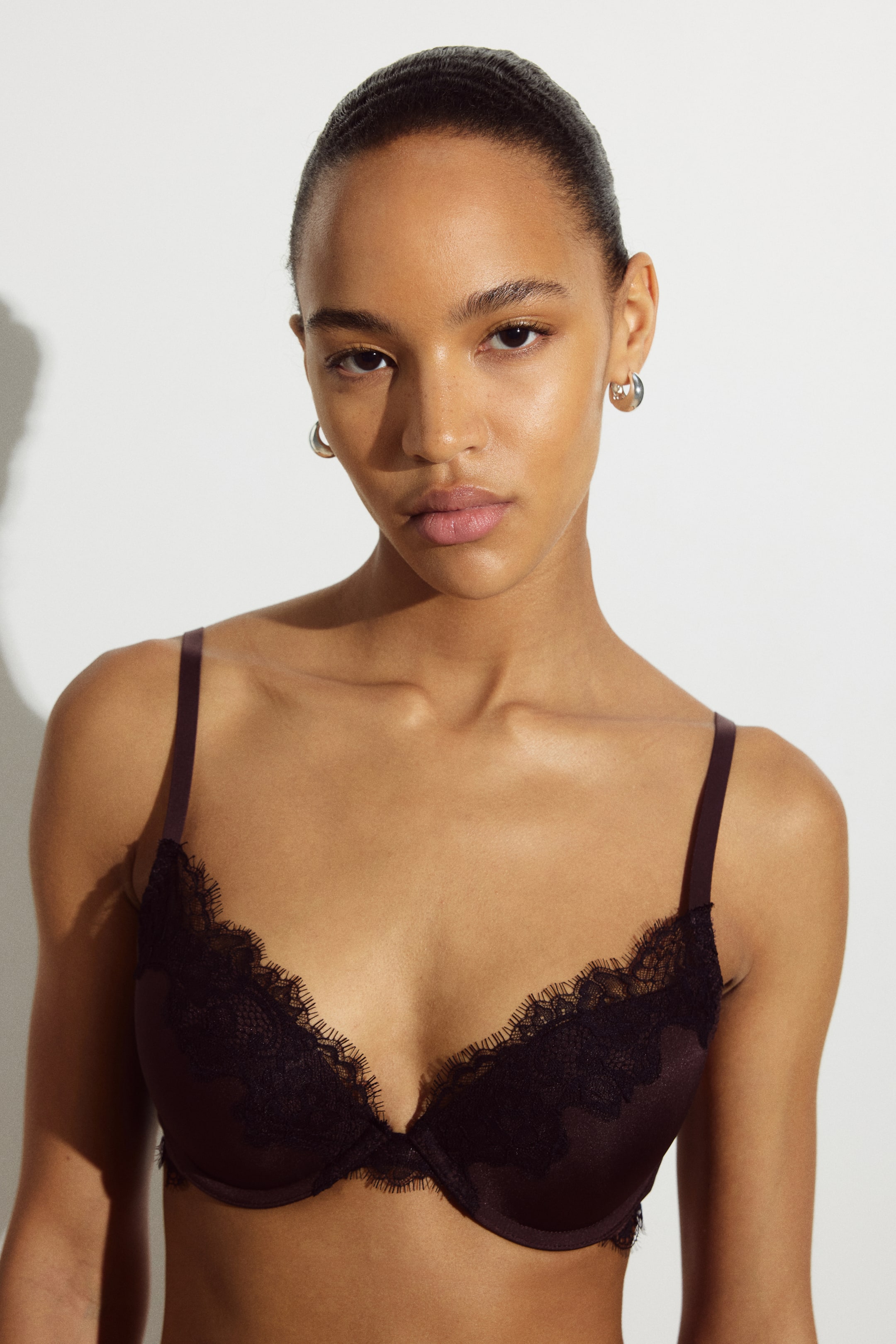 View larger image: A dark brown microfibre push-up bra with delicate black lace trim along the cups is being worn by the model. The bra features underwired, padded cups and thin, adjustable shoulder straps.