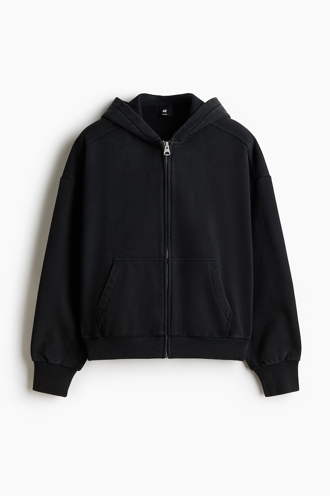 The black zip-up hoodie is presenting its front, featuring a full-length metal zipper, a hood, two front kangaroo pockets, and ribbed cuffs and hem. - 1