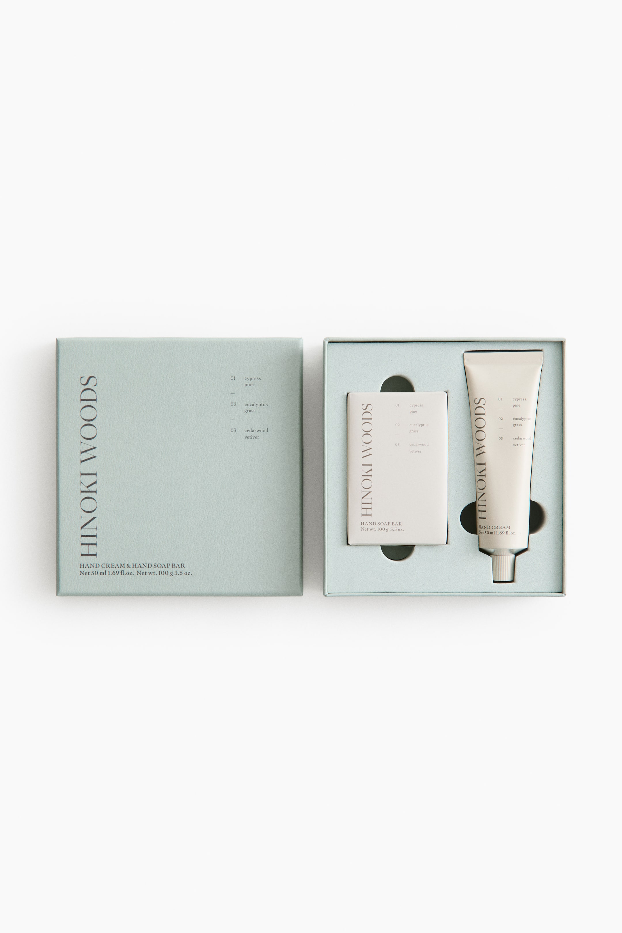 Ver imagen más grande: Un set de regalo de crema de manos y jabón en barra de Hinoki Woods en color verde claro se exhibe. La caja cerrada presenta detalles del producto, incluyendo descripciones de fragancias, mientras que la caja abierta revela una barra de jabón de manos blanca y un tubo de crema de manos blanca con tapa plateada, ambos acomodados en compartimentos personalizados.