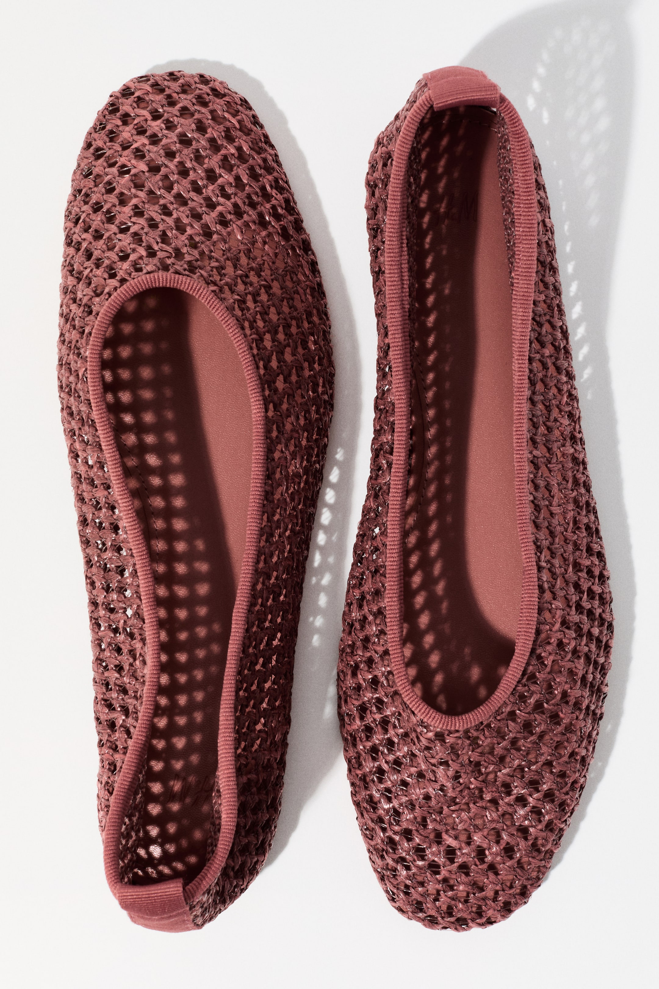 View larger image: A pair of muted rose flat shoes is showcased from an overhead view, highlighting an open-weave mesh upper and a smooth interior. An elasticized trim outlines the opening, and a small pull tab is visible at each heel.
