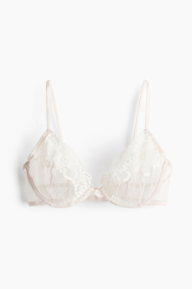 Frontaal weergegeven off-white beha met doorschijnende polkadot-meshcups en een geschulpte bloemenkant-overlay. De beha toont een zichtbare beugelconstructie, dunne verstelbare bandjes en een subtiele rozeachtig-beige bies langs de randen. - 1