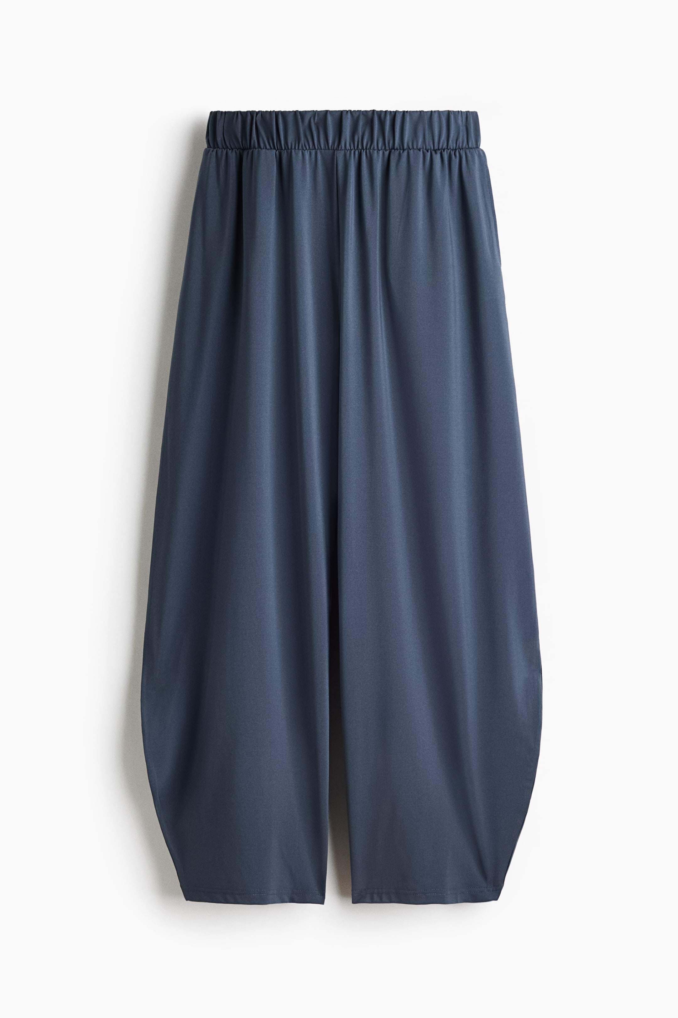 View larger image: Slate blue trousers are facing front, showcasing a gathered elastic waistband and a relaxed, wide-legged fit with curved outer leg hems.