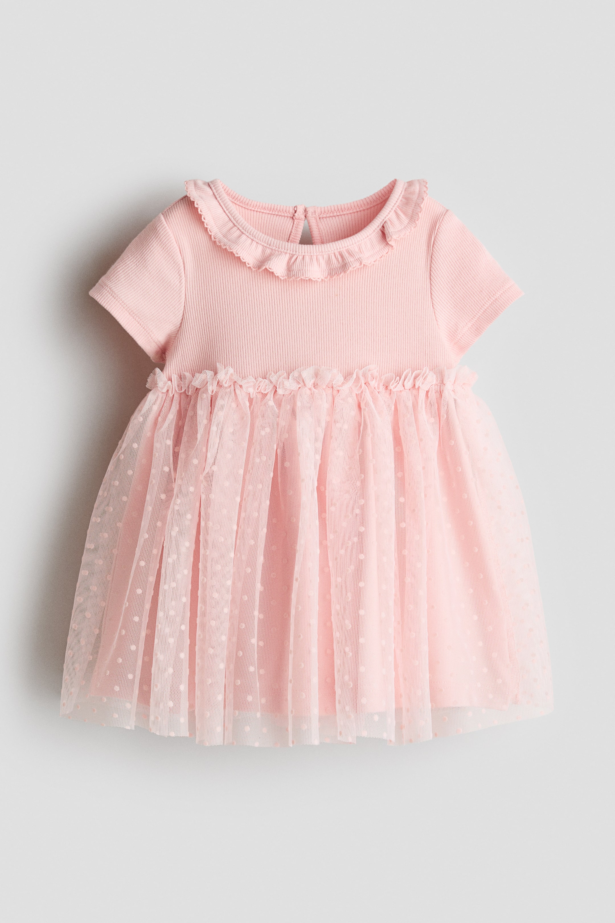 View larger image: A pink baby dress showcases a ribbed knit bodice with short sleeves and a ruffled round collar. A ruffled seam divides the bodice from the full skirt, which highlights an outer layer of sheer polka-dotted tulle over a solid pink underskirt.