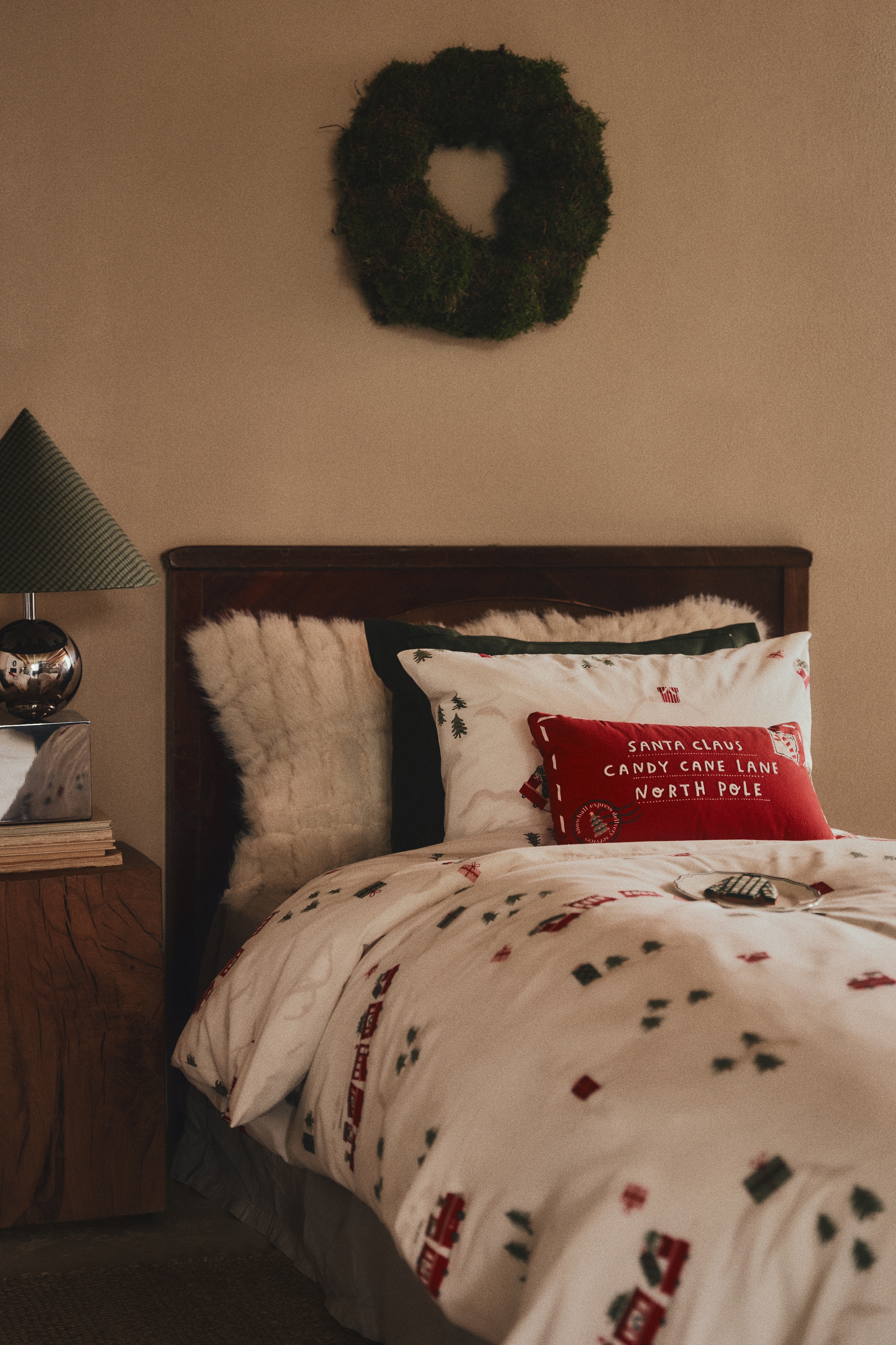 A red rectangular throw pillow is displaying a front-facing design resembling a letter to Santa Claus. The pillow features white embroidered text in the centre that reads "SANTA CLAUS / CANDY CANE LANE / NORTH POLE," framed by a dashed white border. A candy cane postage stamp applique details the top-right corner, while a circular postmark graphic appears in the bottom-left corner.