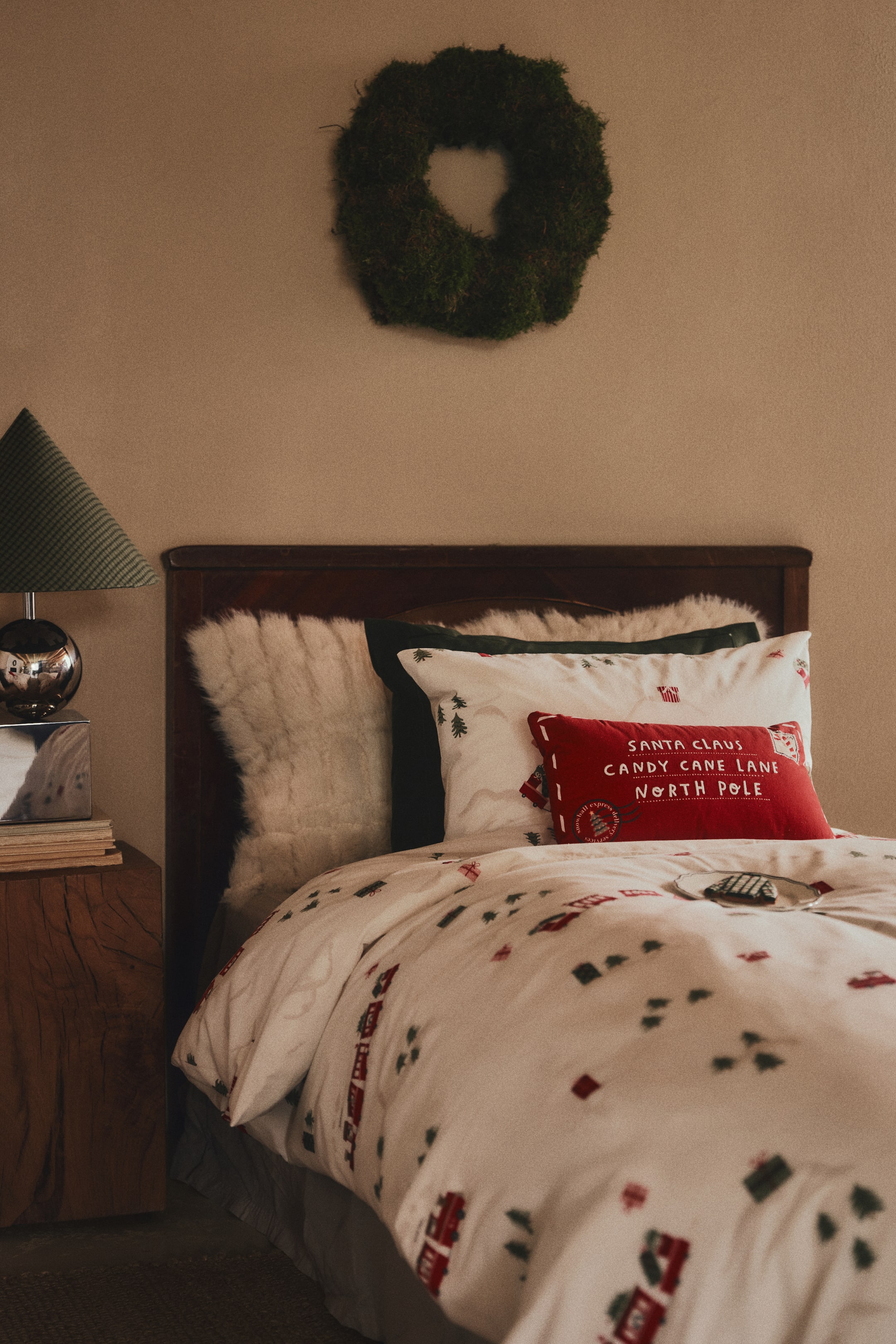 View larger image: A rectangular red cotton canvas cushion, designed to resemble a festive letter to Santa, is resting on a bed and shown from the front. It features white embroidered text reading "SANTA CLAUS, CANDY CANE LANE, NORTH POLE" along with printed stamp and postmark details.