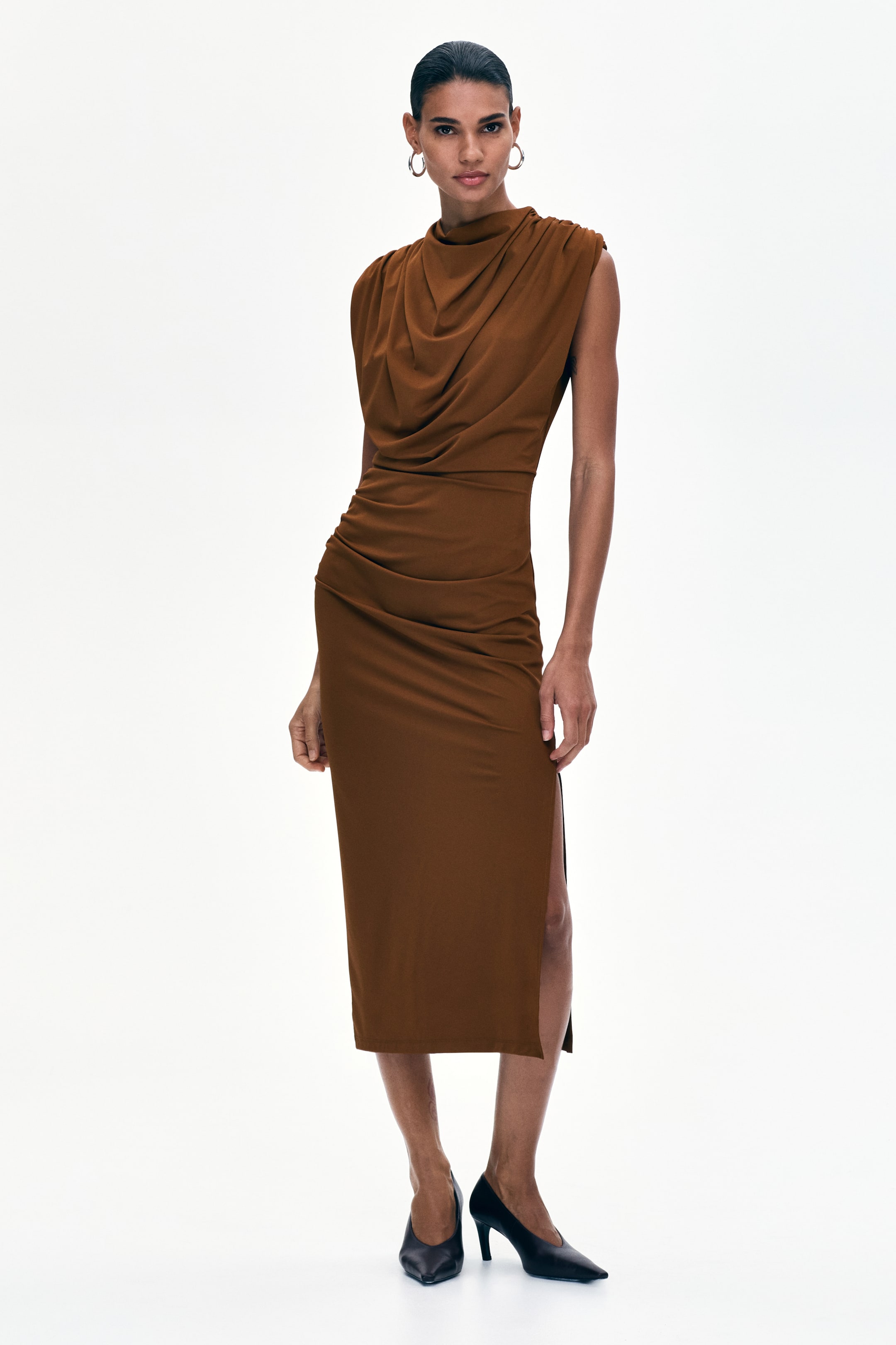 View larger image: A brown midi dress featuring a draped cowl neckline and a sleeveless design, presenting a fitted silhouette with ruched detailing on the left hip and a side slit on the left leg.